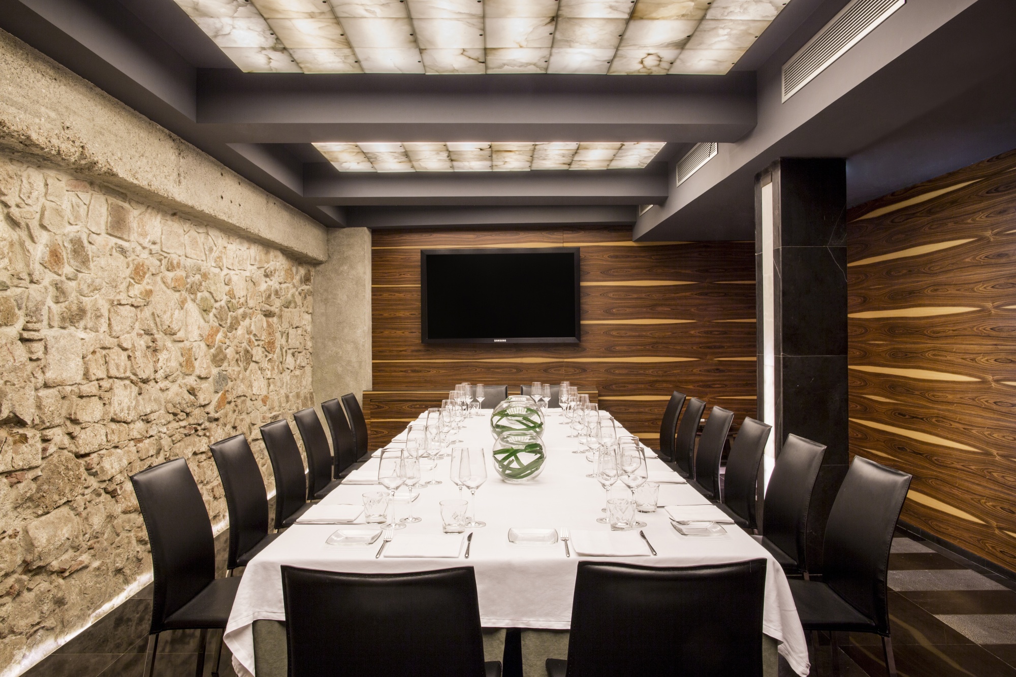 Una mesa larga con mantel y sillas rodeada de paredes de piedra y paneles de madera, vista desde el interior de la sala.