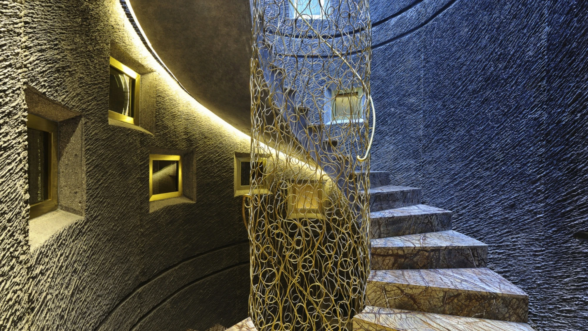 Se ve una escalera interior con peldaños claros, una pared oscura y luces empotradas a ambos lados.