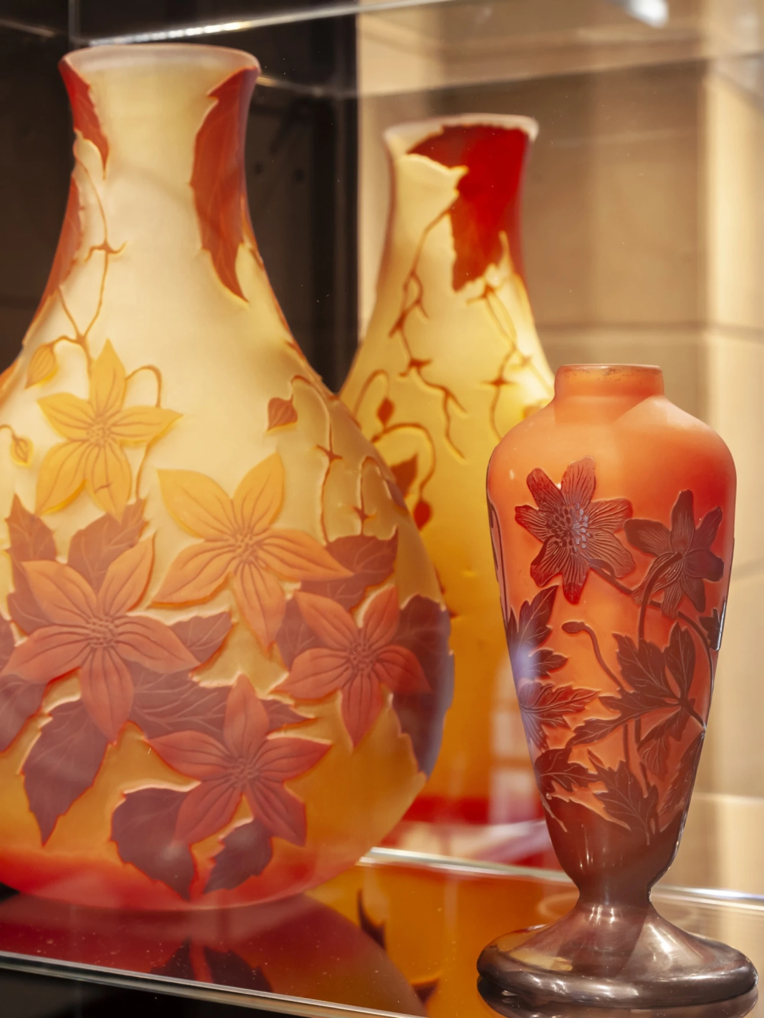Se observan dos jarrones decorativos de colores con motivos florales sobre una vitrina iluminada.