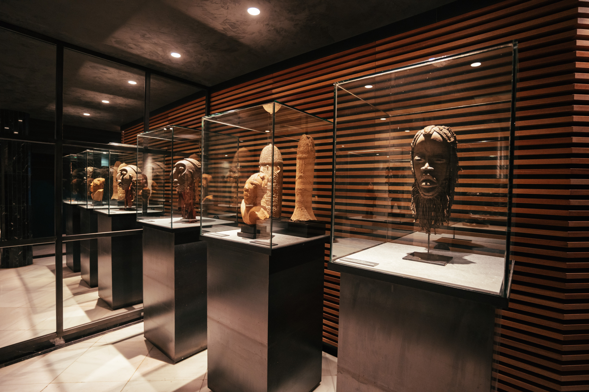 Se ve una sala de exposición con vitrinas y esculturas sobre pedestales, iluminada con luces empotradas.