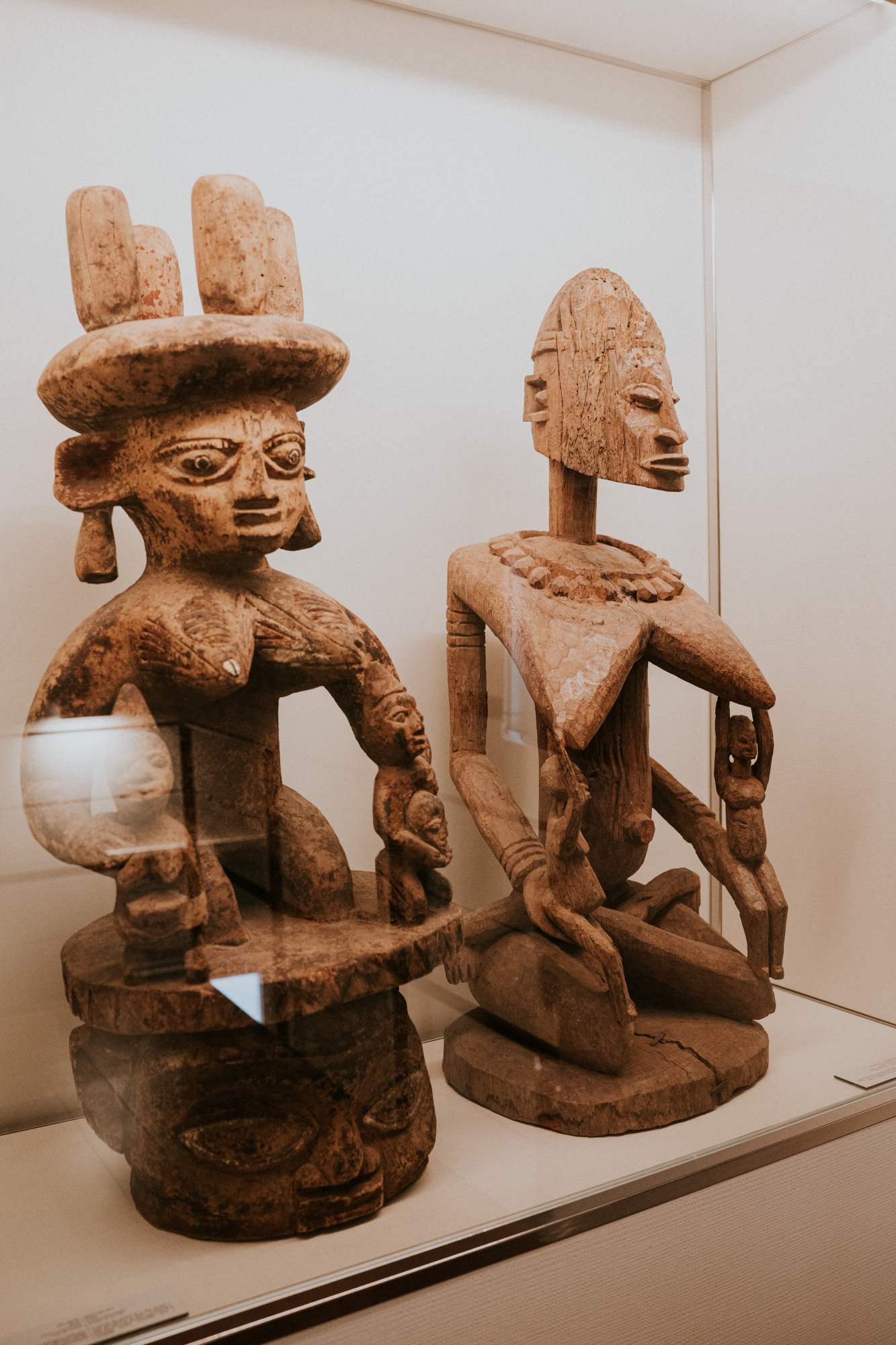 Se observan dos esculturas africanas de madera sobre una vitrina en una sala de exposición.