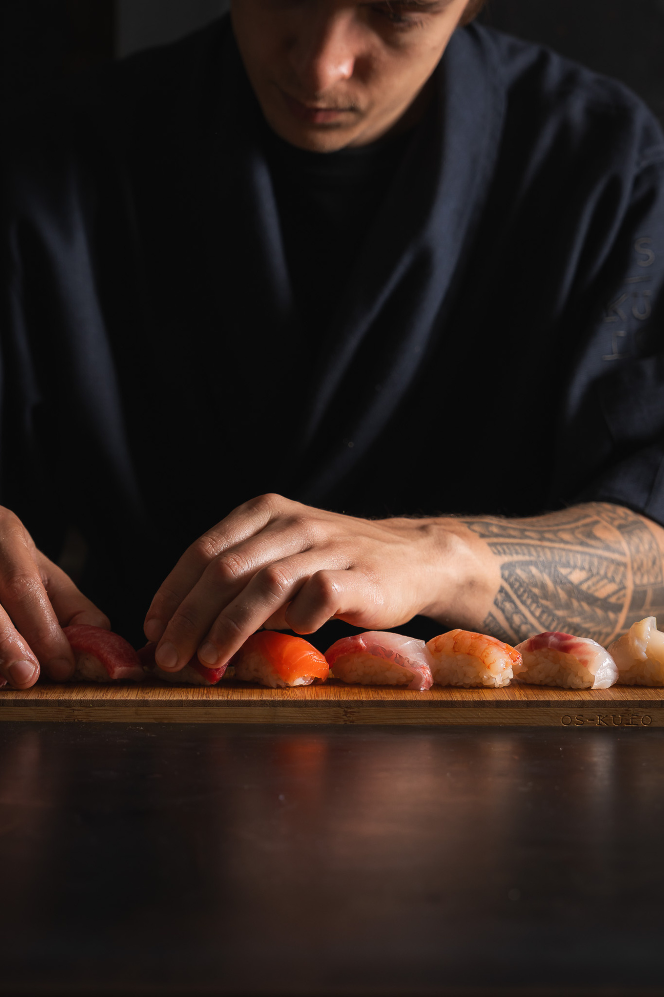 El chef prepara nigiris sobre una tabla de madera con piezas de sushi alineadas.