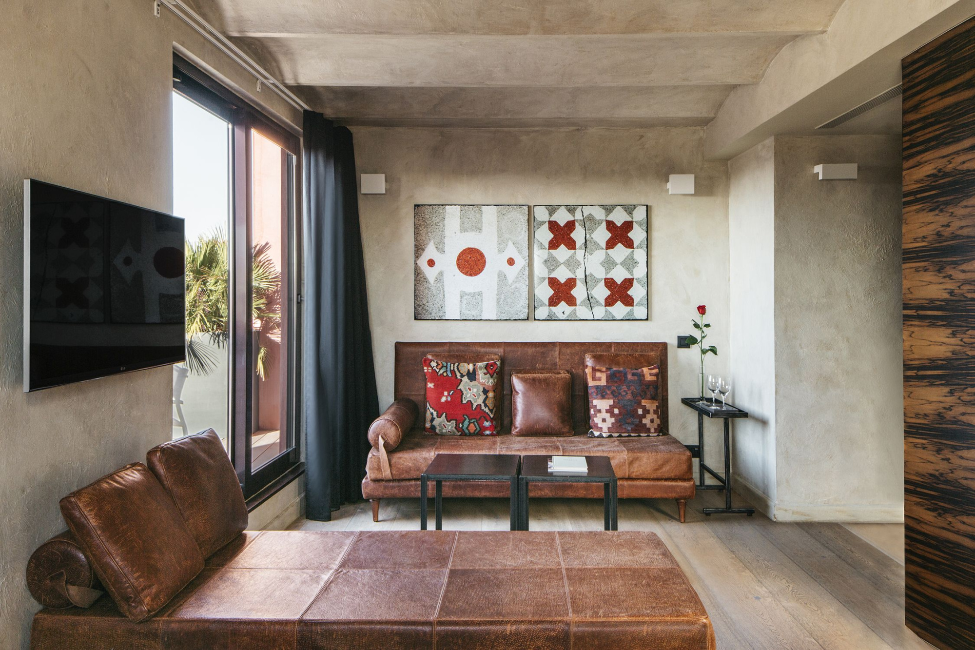 Salón con sofá de cuero, mesa baja, pared decorada y puertas de vidrio con cortinas.