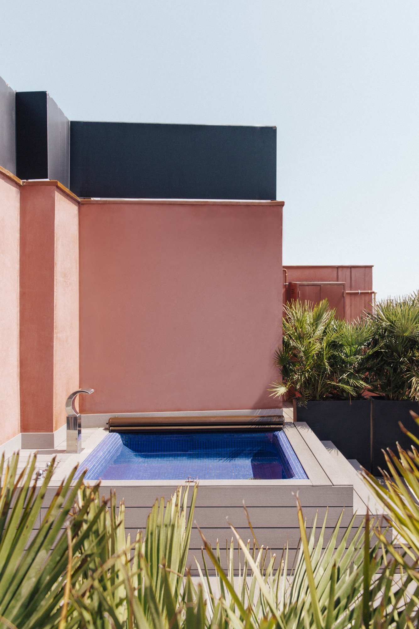 Se ve una piscina pequeña en un patio con paredes claras y vegetación alrededor.