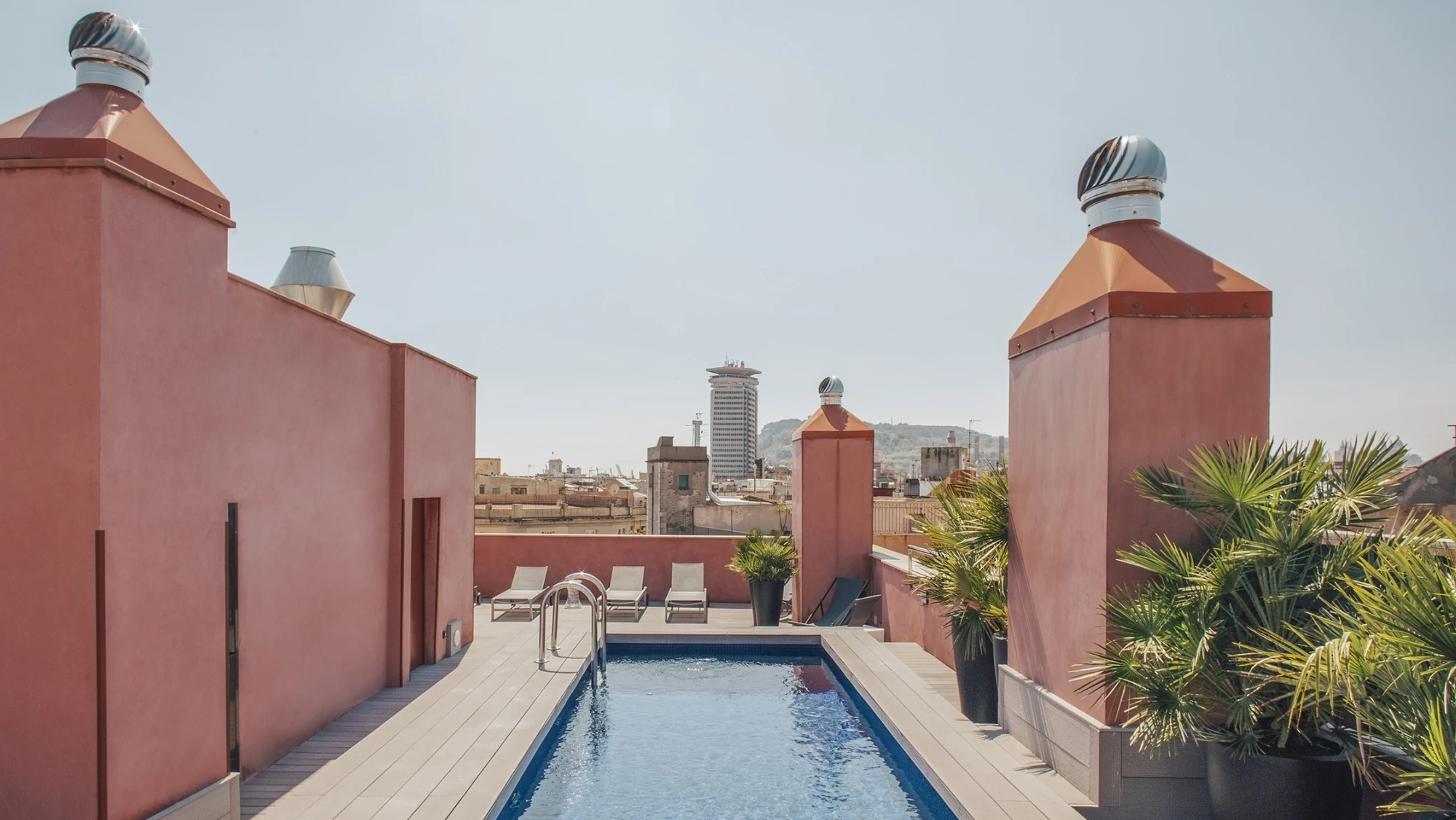 Se ve una piscina rectangular en una terraza con paredes de color rojo y plantas decorativas.