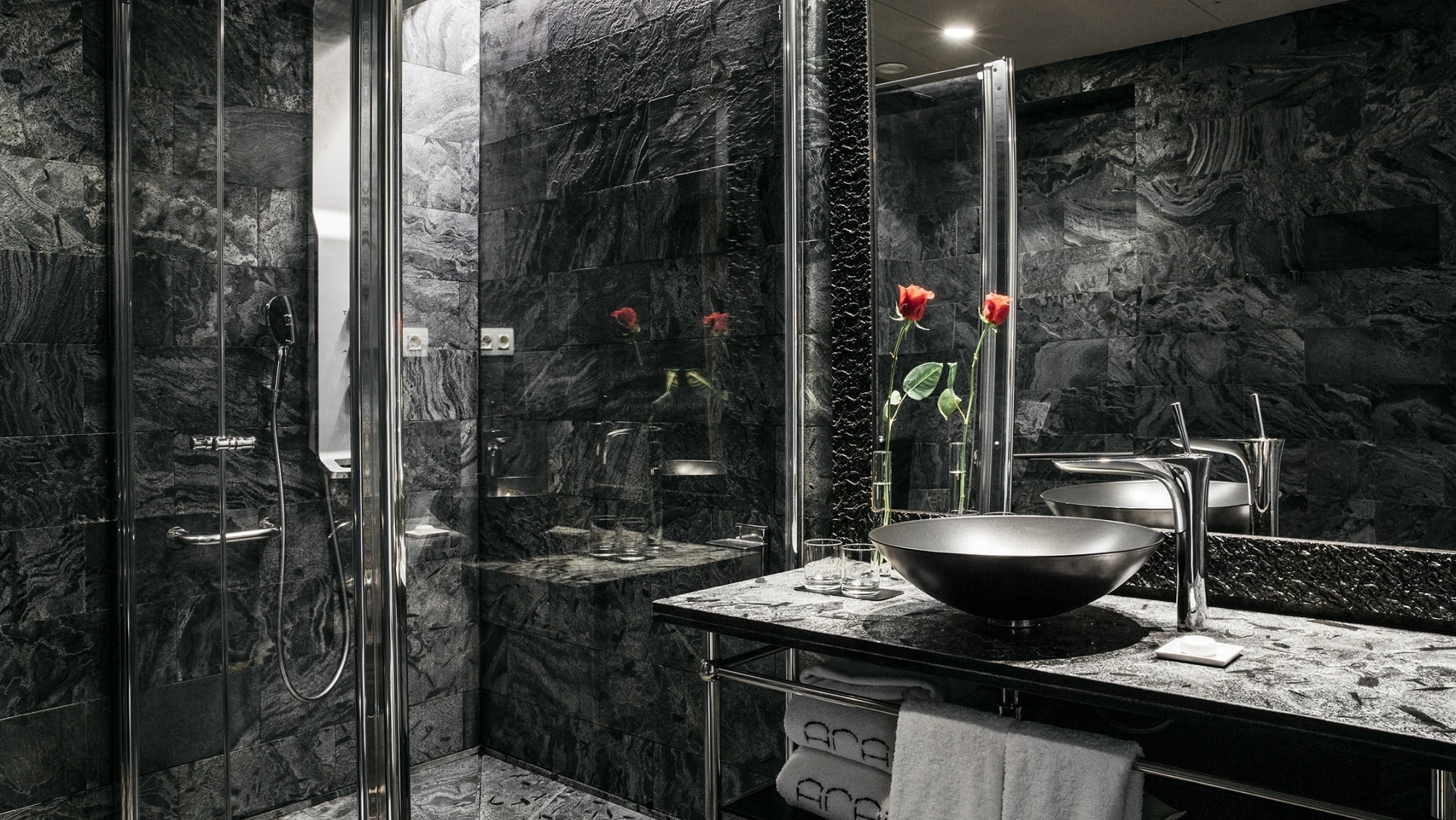 Se ve un baño moderno con ducha de vidrio, lavabo y encimera de piedra oscura.