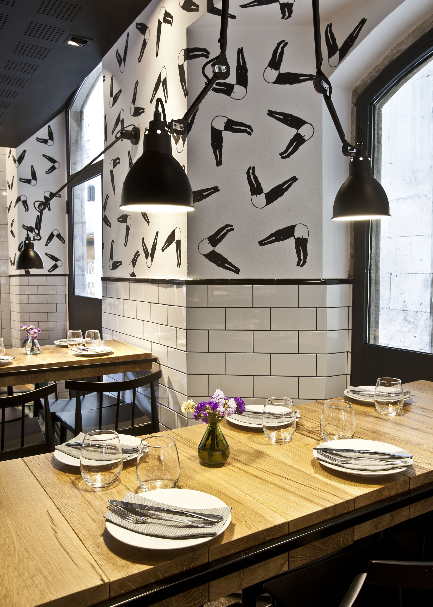 Se ve un comedor con una mesa de madera preparada con platos y vasos, y una pared decorada con lámparas colgantes.