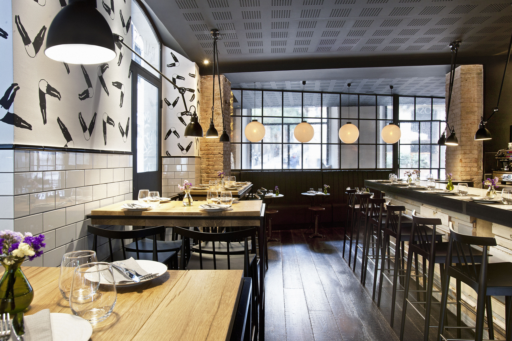 El comedor muestra mesas con vajilla, sillas y lámparas colgantes sobre un suelo de madera.