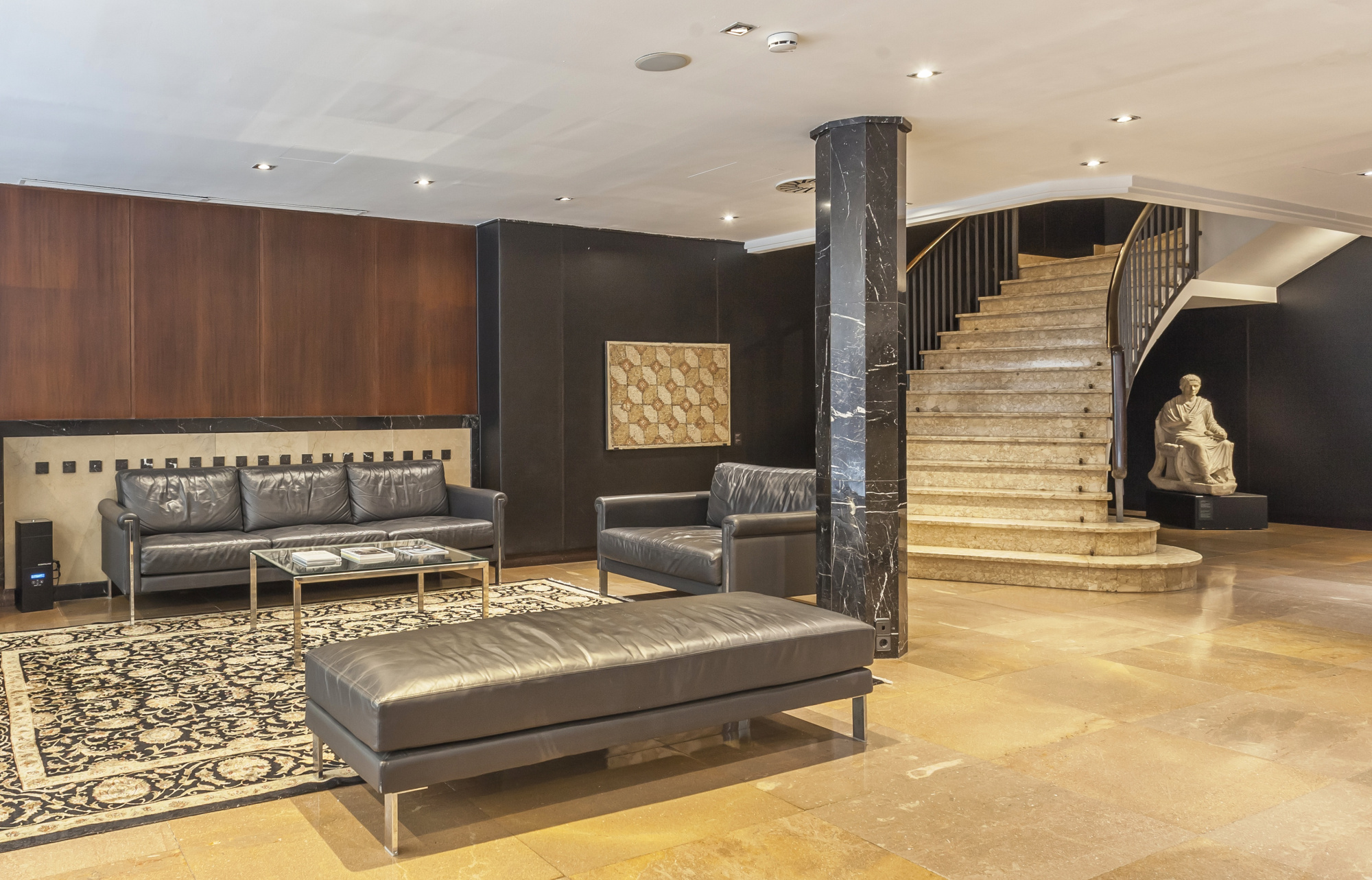 Se ve una zona de estar con sofás y una escalera de madera en un espacio interior iluminado.