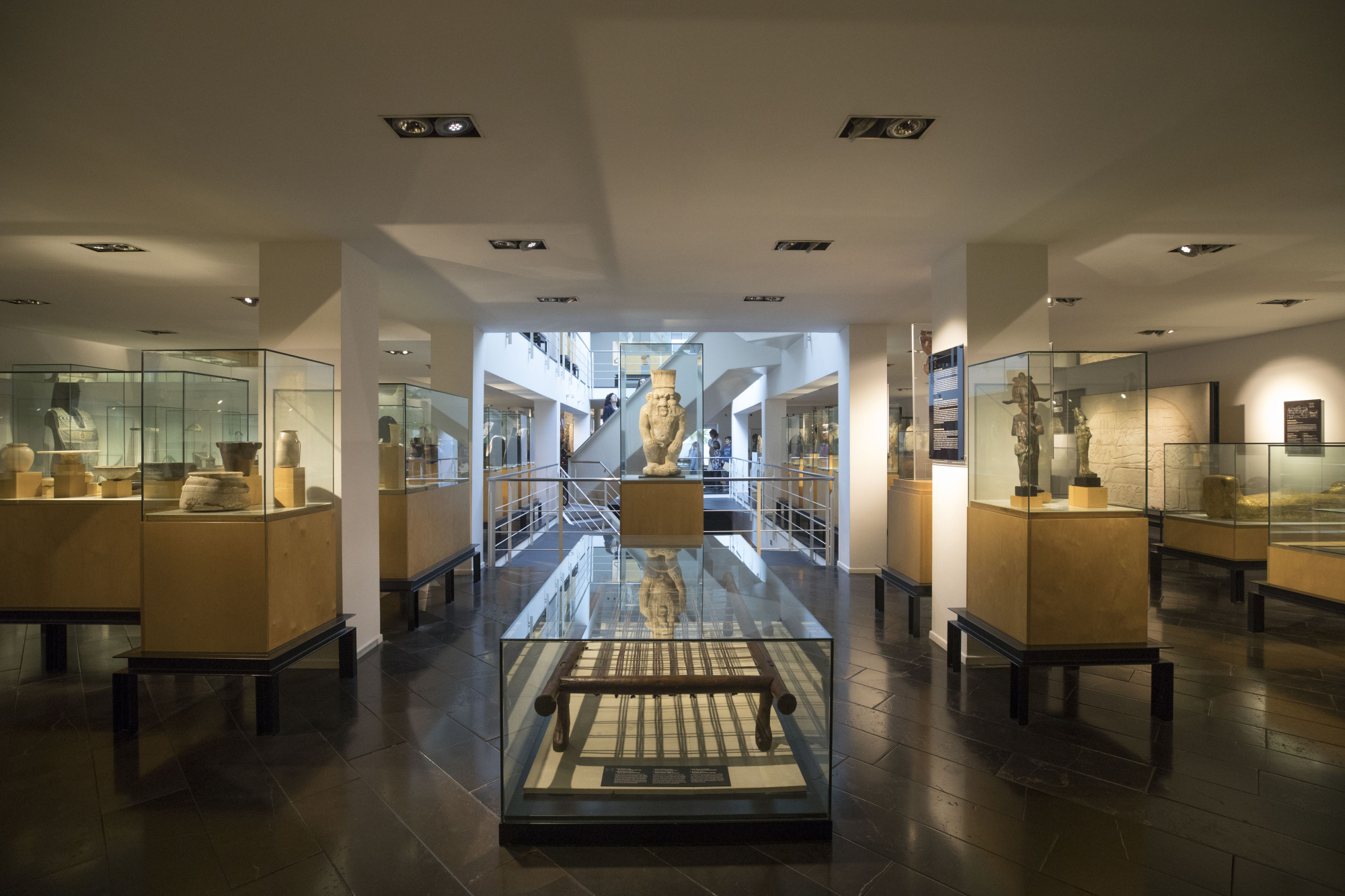 Interior del Museu Egipci de Barcelona.
Vitrines amb objectes arqueològics exposats i escales centrals blanques que comunican les 3 plantes d'exposició i la terrassa.