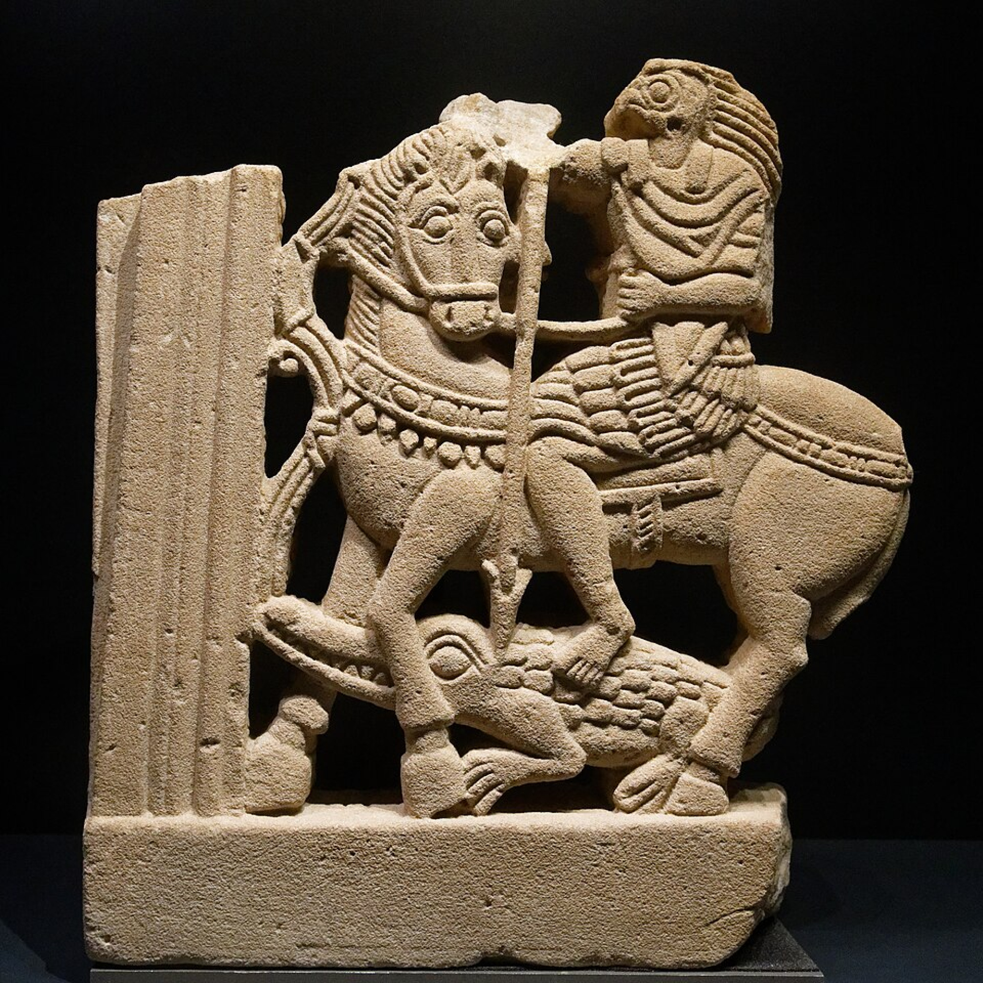 Una escultura de un caballero con armadura, representando a Horus, ubicada en el Louvre. La pieza es de estilo clásico, con detalles en tonos dorados y una postura imponente.