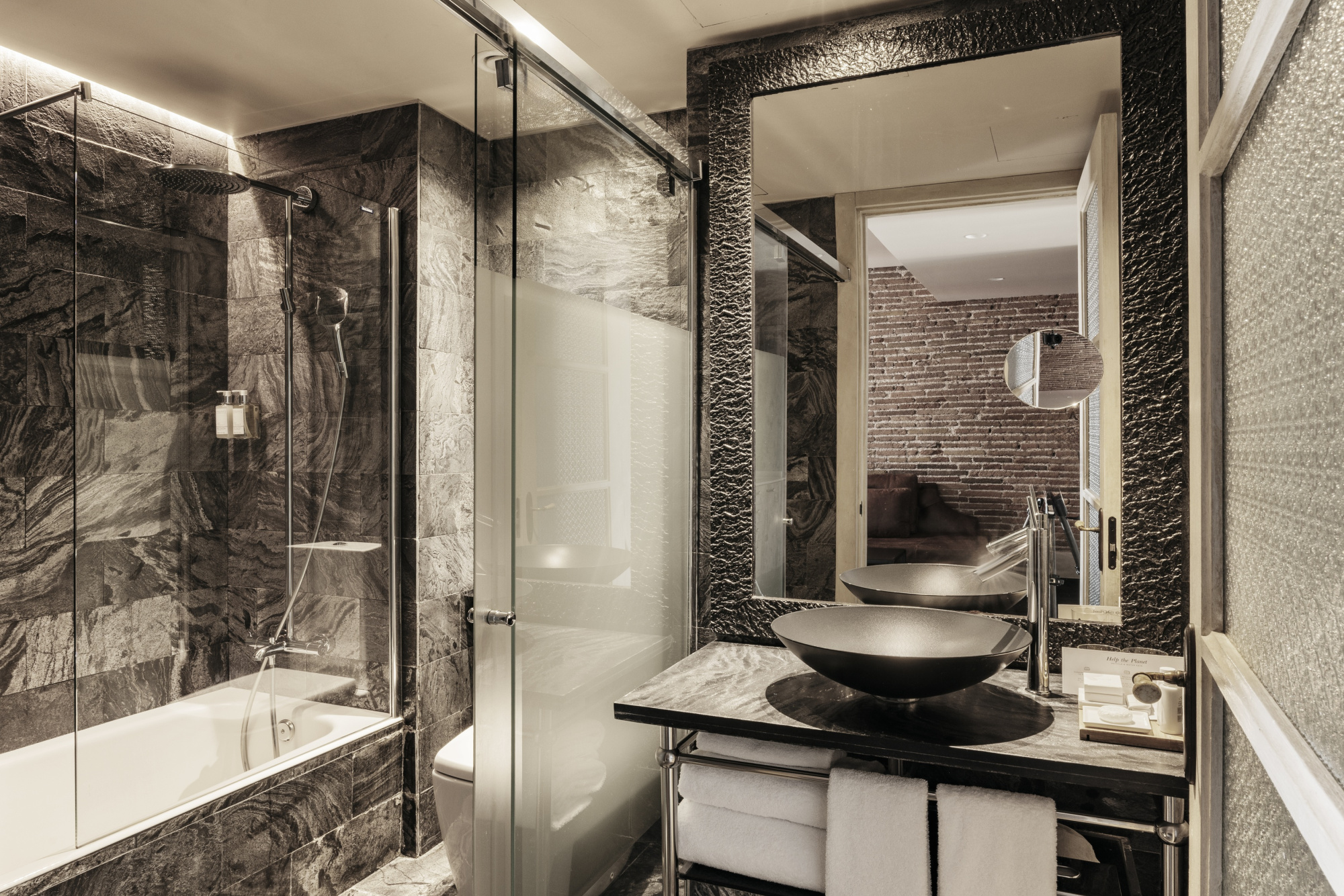Baño moderno con ducha de cristal, lavabo negro y paredes con azulejos grises.