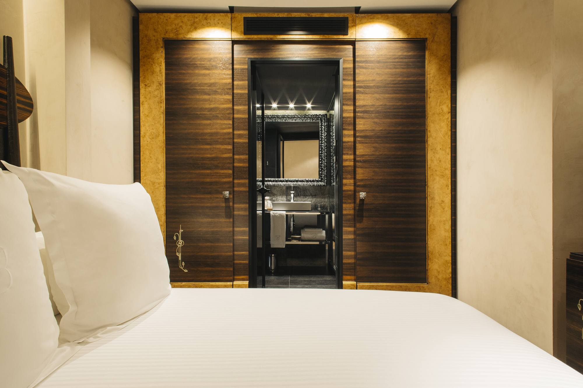 Una habitación con una cama con sábanas blancas y un espejo rectangular decorativo en la pared.