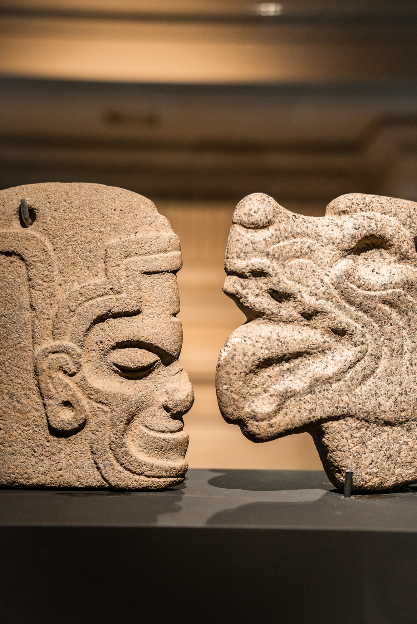 Dos esculturas de piedra decorativas se exhiben sobre un soporte en una sala interior.