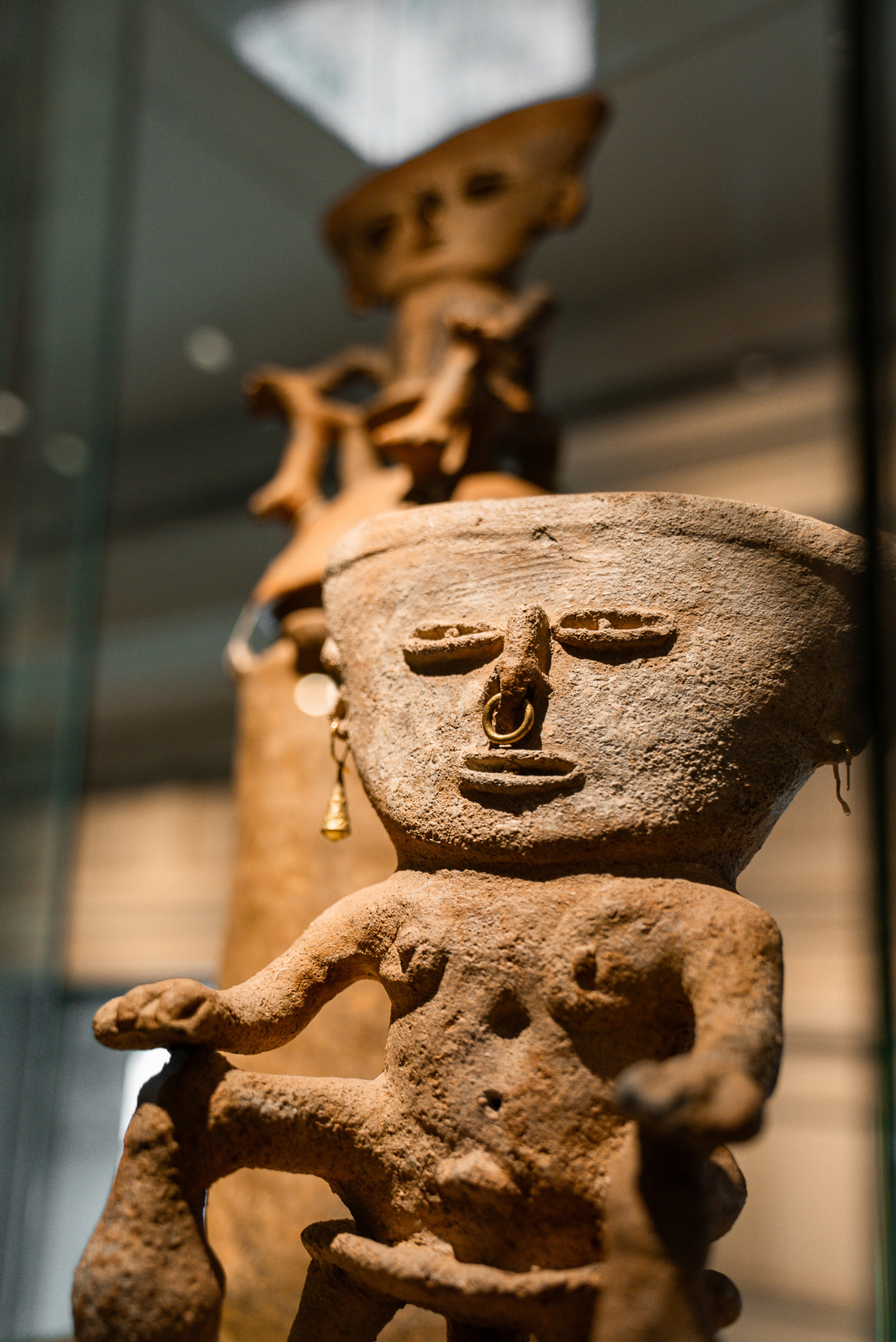 Se ve una escultura de figura humana de estilo antiguo sobre una base de piedra en un espacio interior.