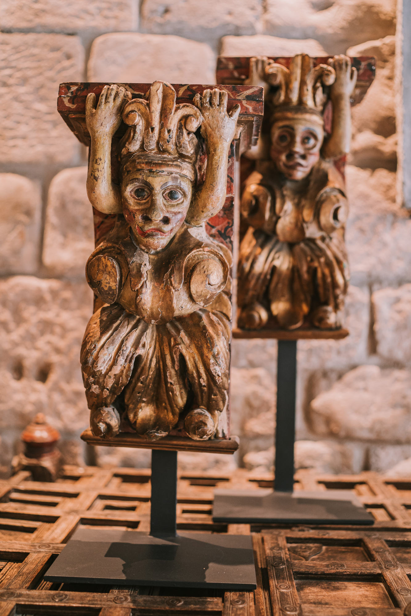 Se ven varias esculturas de estilo figurativo sobre pedestales frente a un muro de piedra.