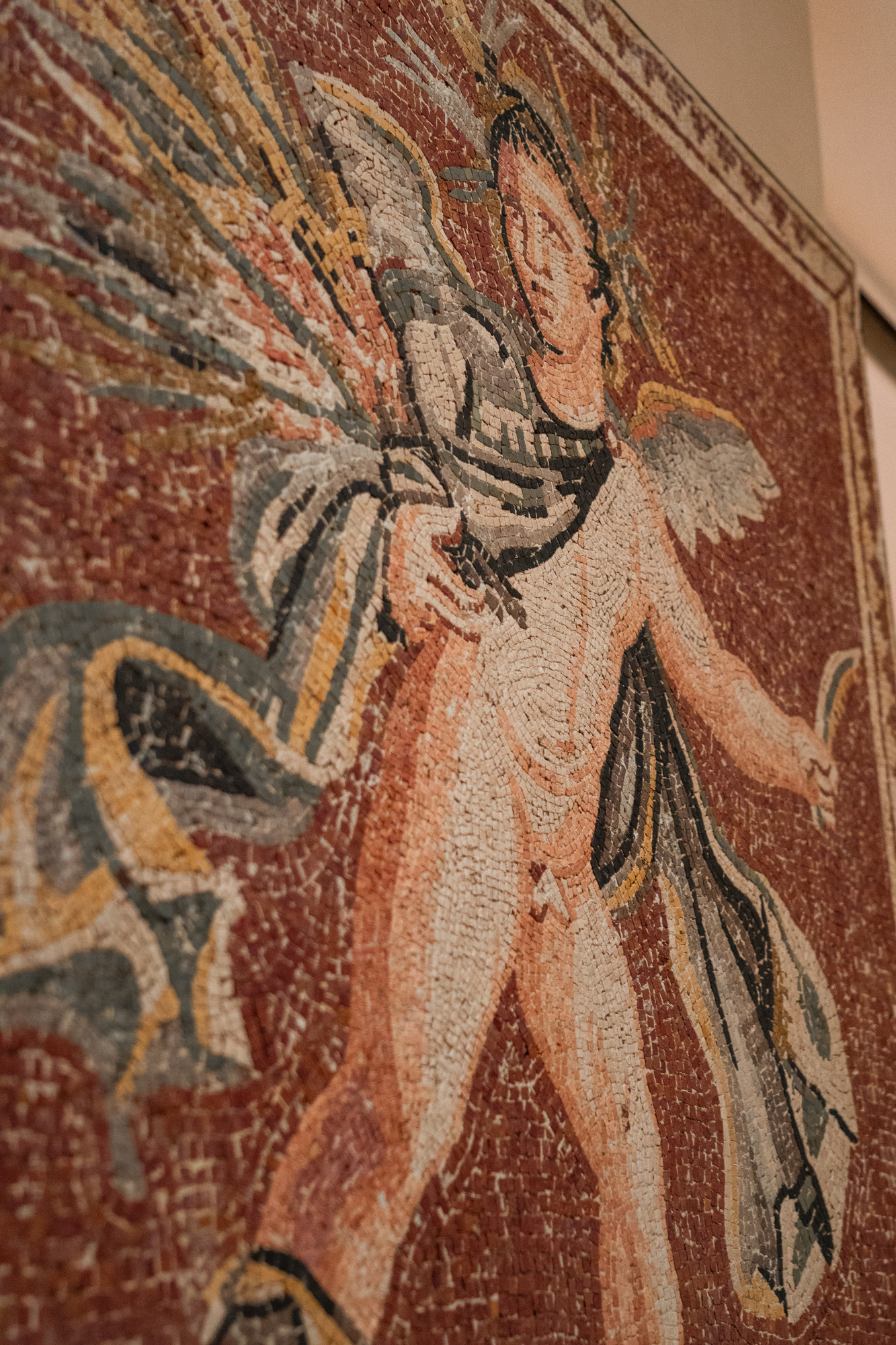 Se ve un mosaico decorativo con una figura humana y motivos geométricos sobre un fondo rojizo.