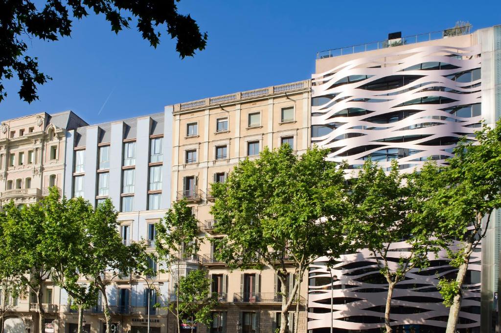 Se ve la fachada de un edificio moderno con árboles verdes delante y un cielo azul de fondo.
