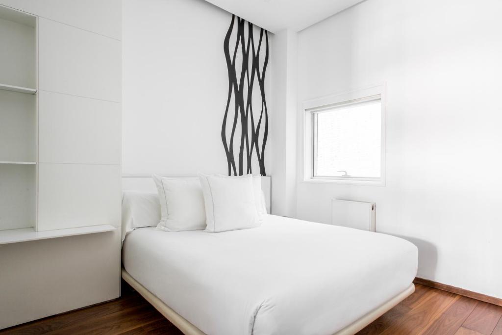 Se ve una cama doble con almohadas y un radiador junto a una ventana en una habitación blanca.