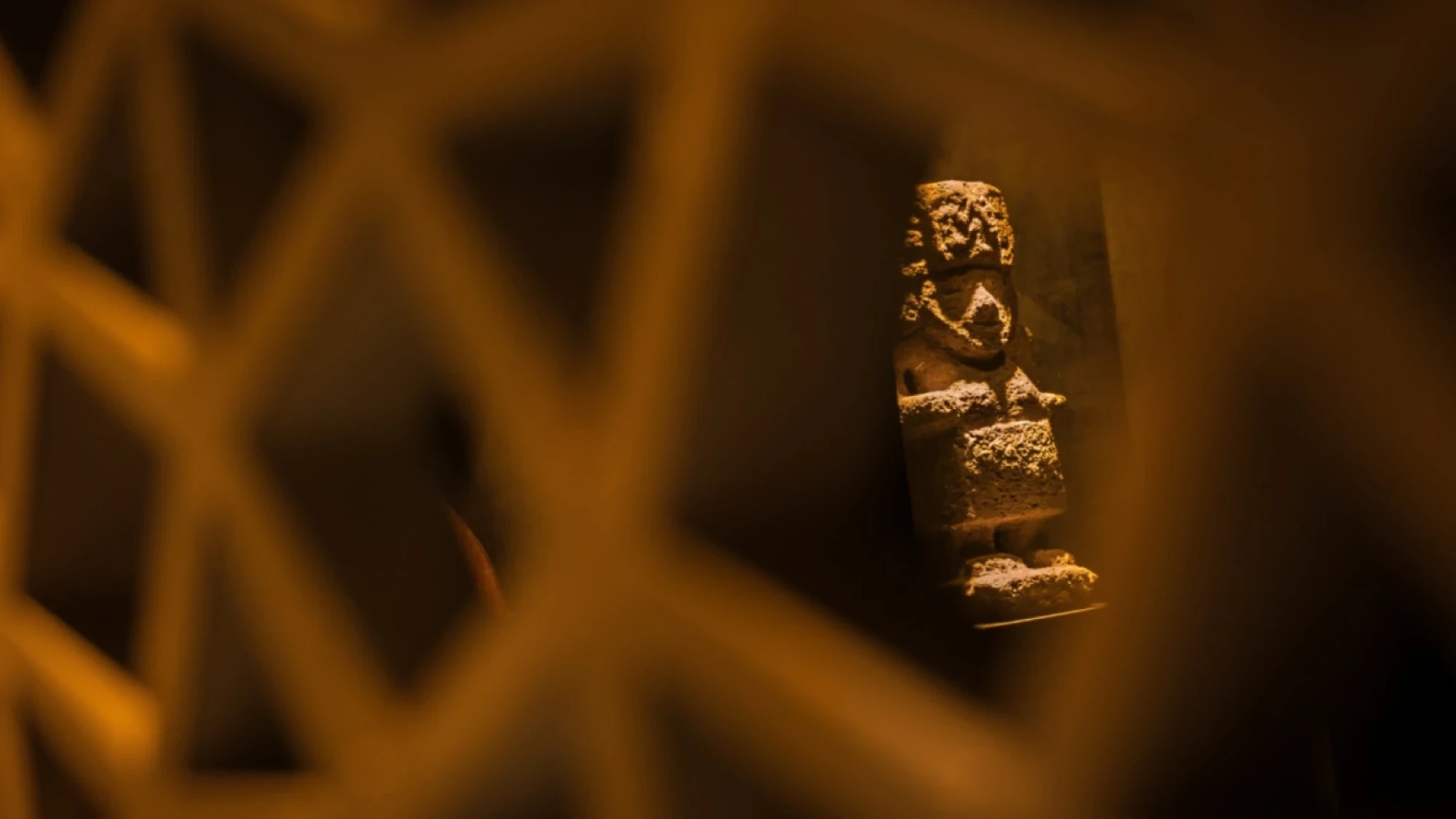 Se ve una pequeña estatua decorativa sobre un fondo oscuro y una estructura geométrica desenfocada.