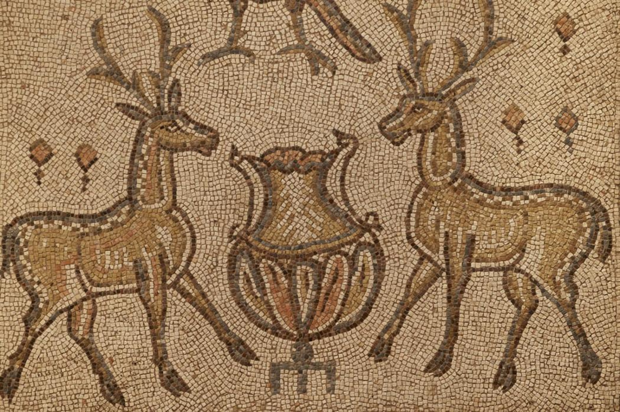 Se aprecia un mosaico romano con ciervos y figuras decorativas sobre un fondo de piedra.