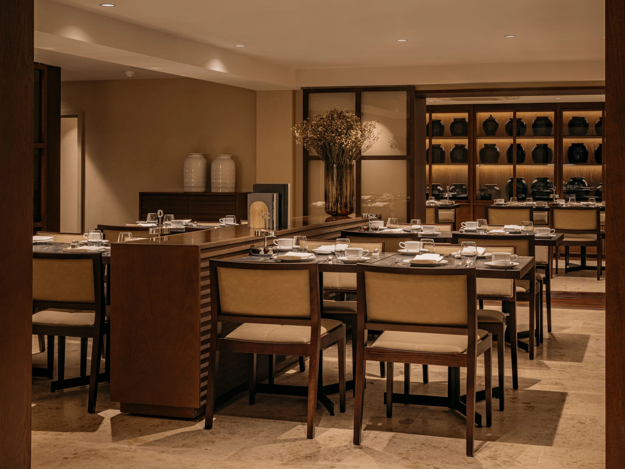 Se ve un comedor con mesas preparadas para el desayuno y una zona de buffet con vajilla y bebidas.