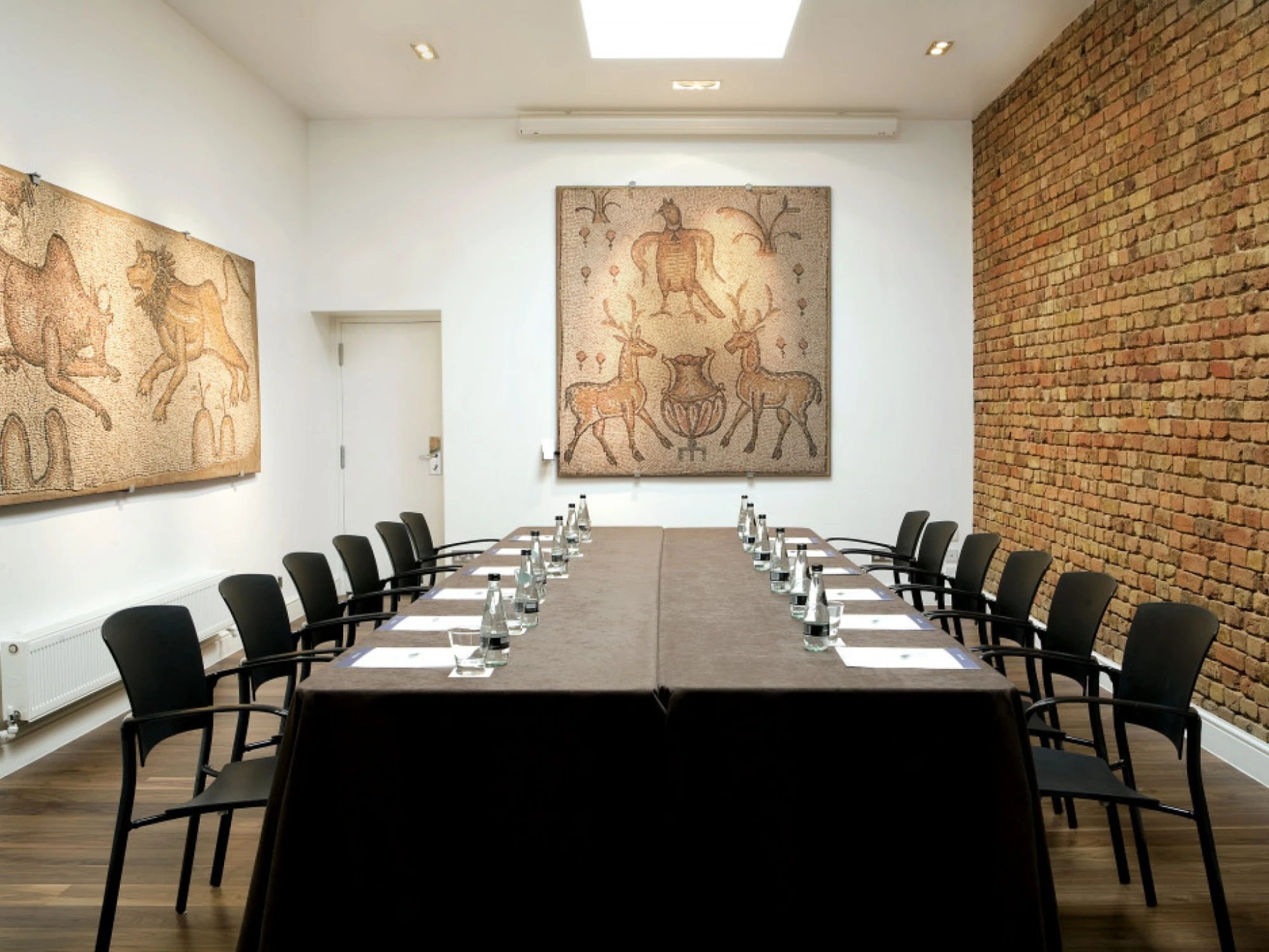 Se ve una sala de reuniones con una mesa larga, sillas y cuadros murales en las paredes de ladrillo.