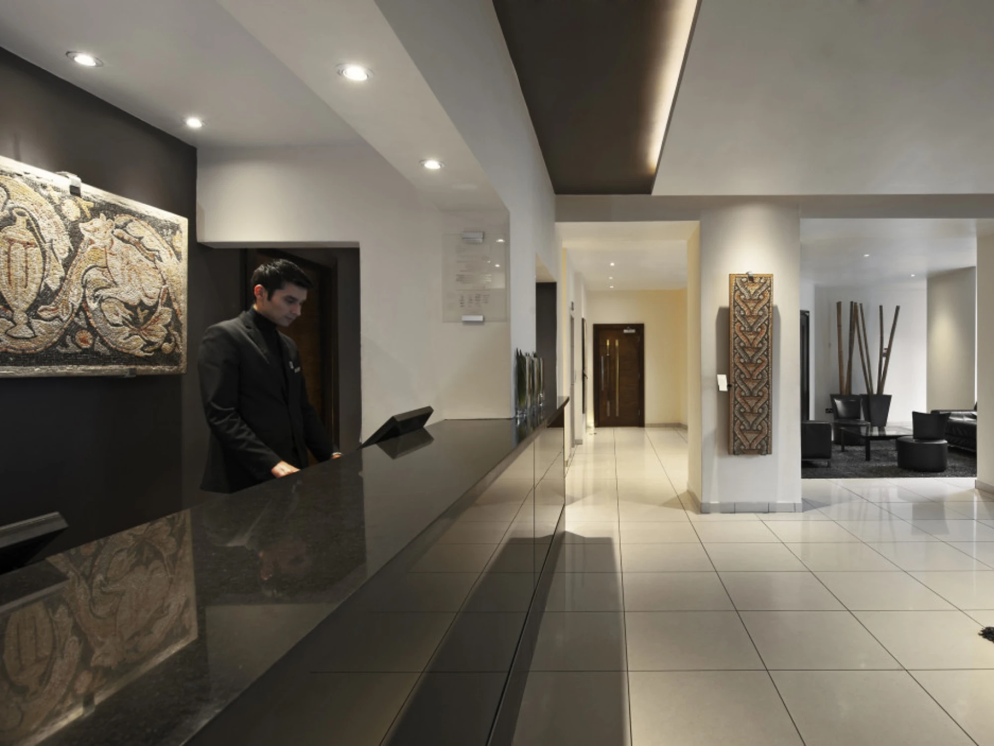 Se ve una recepción interior con mostrador oscuro, iluminación empotrada y un pasillo al fondo.