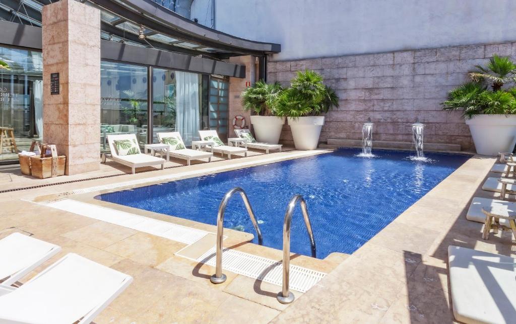 Piscina exterior con tumbonas blancas junto a un edificio de piedra