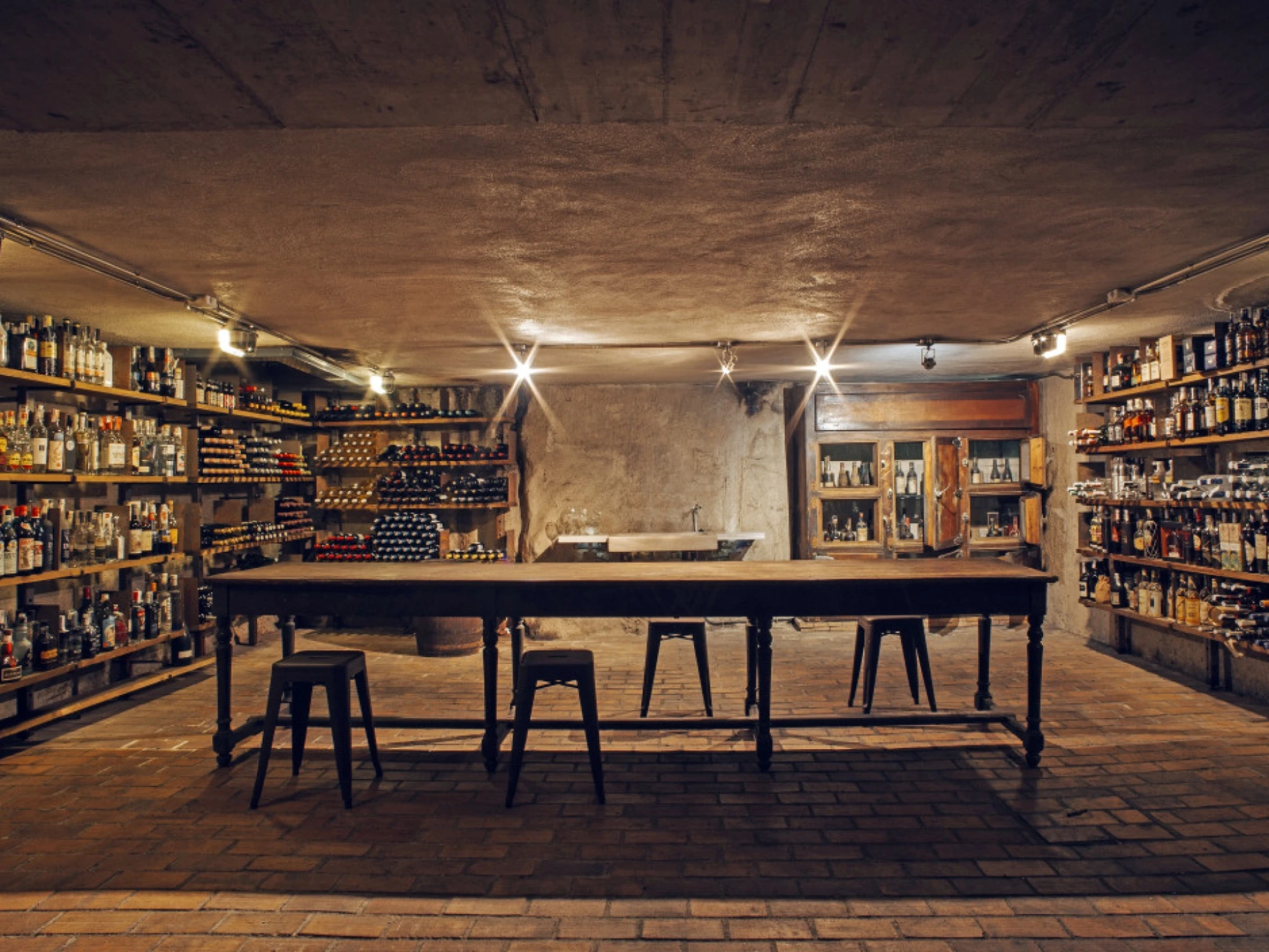 Se ve una cava con estanterías llenas de botellas y una barra central con taburetes.