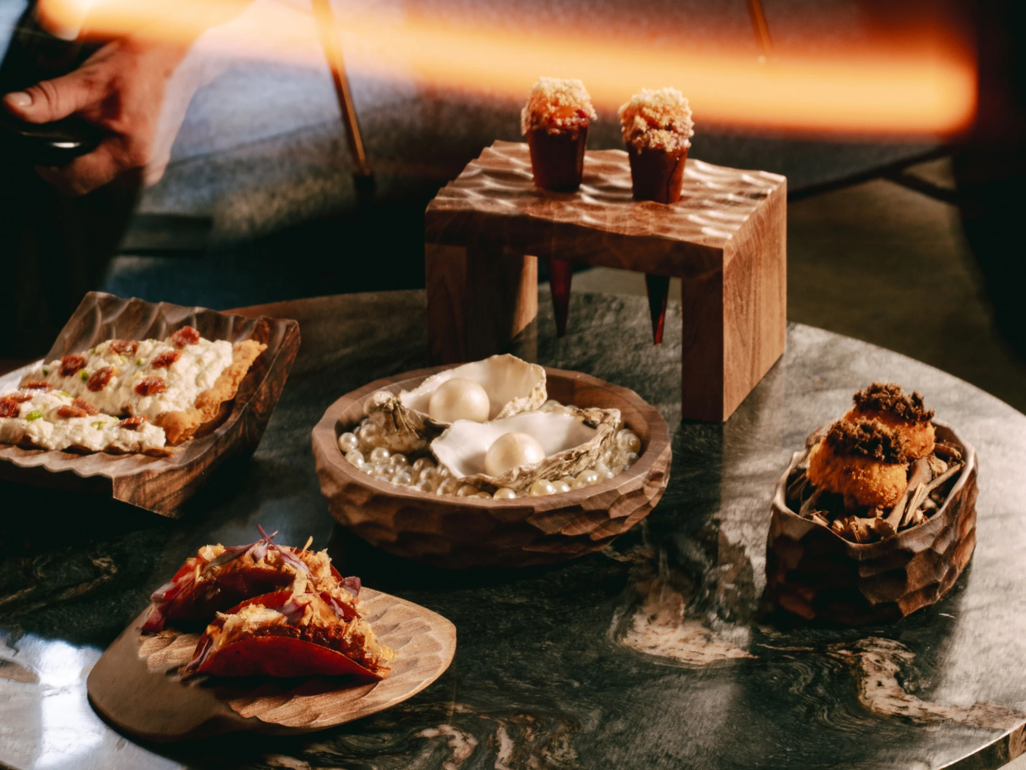 Se ve una mesa con platos de comida, velas encendidas y vasos sobre una superficie de piedra.