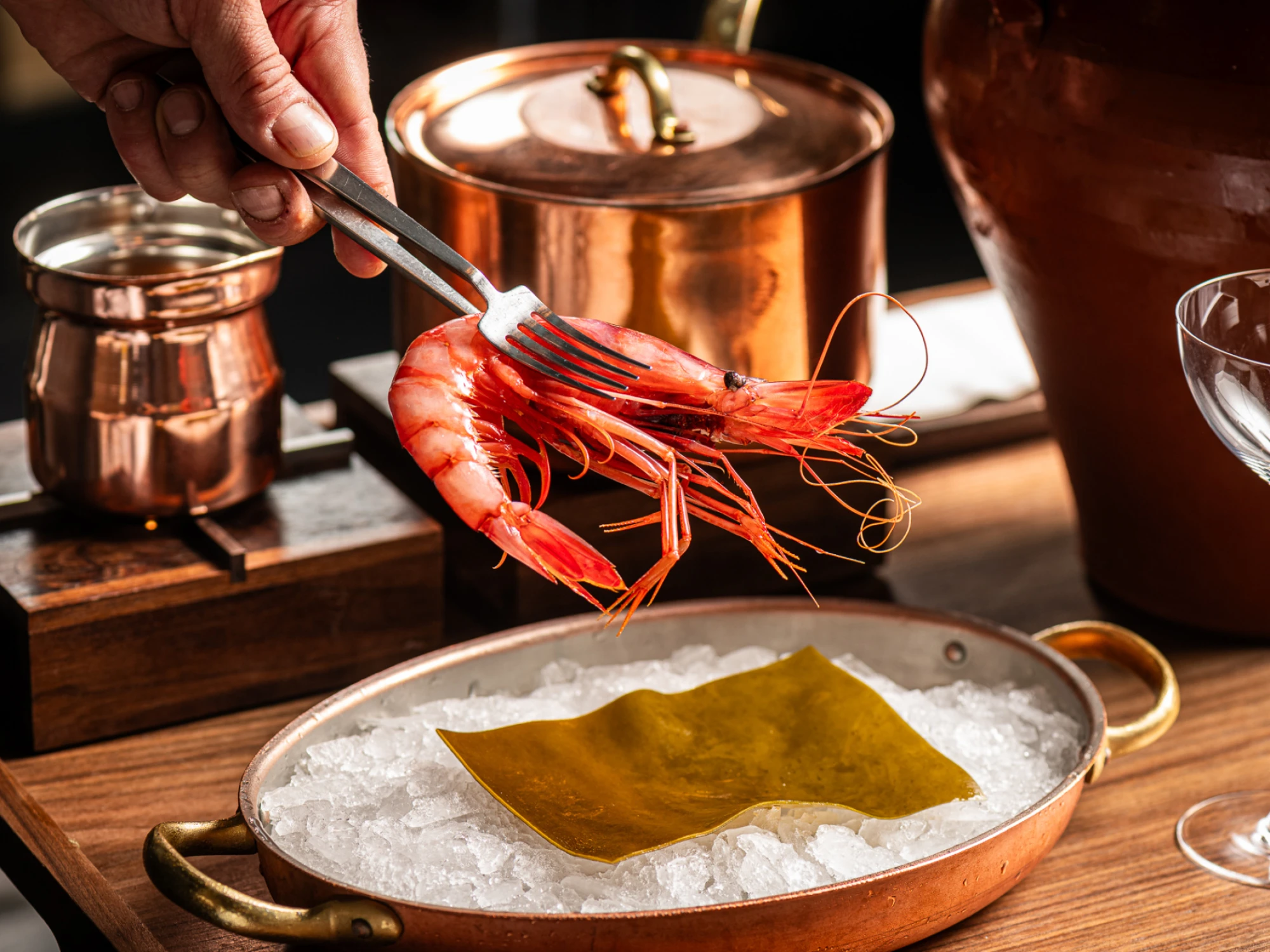 Se ve una gamba roja sobre una bandeja con manteca, mientras se prepara en una cocina con utensilios de cobre.