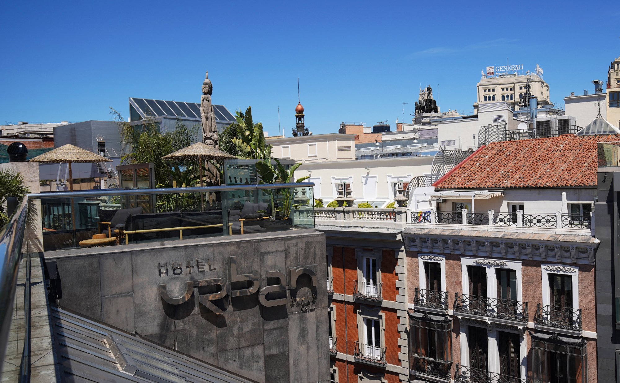 Se ve una terraza con barandilla de piedra y una vista de tejados y edificios bajo un cielo despejado.