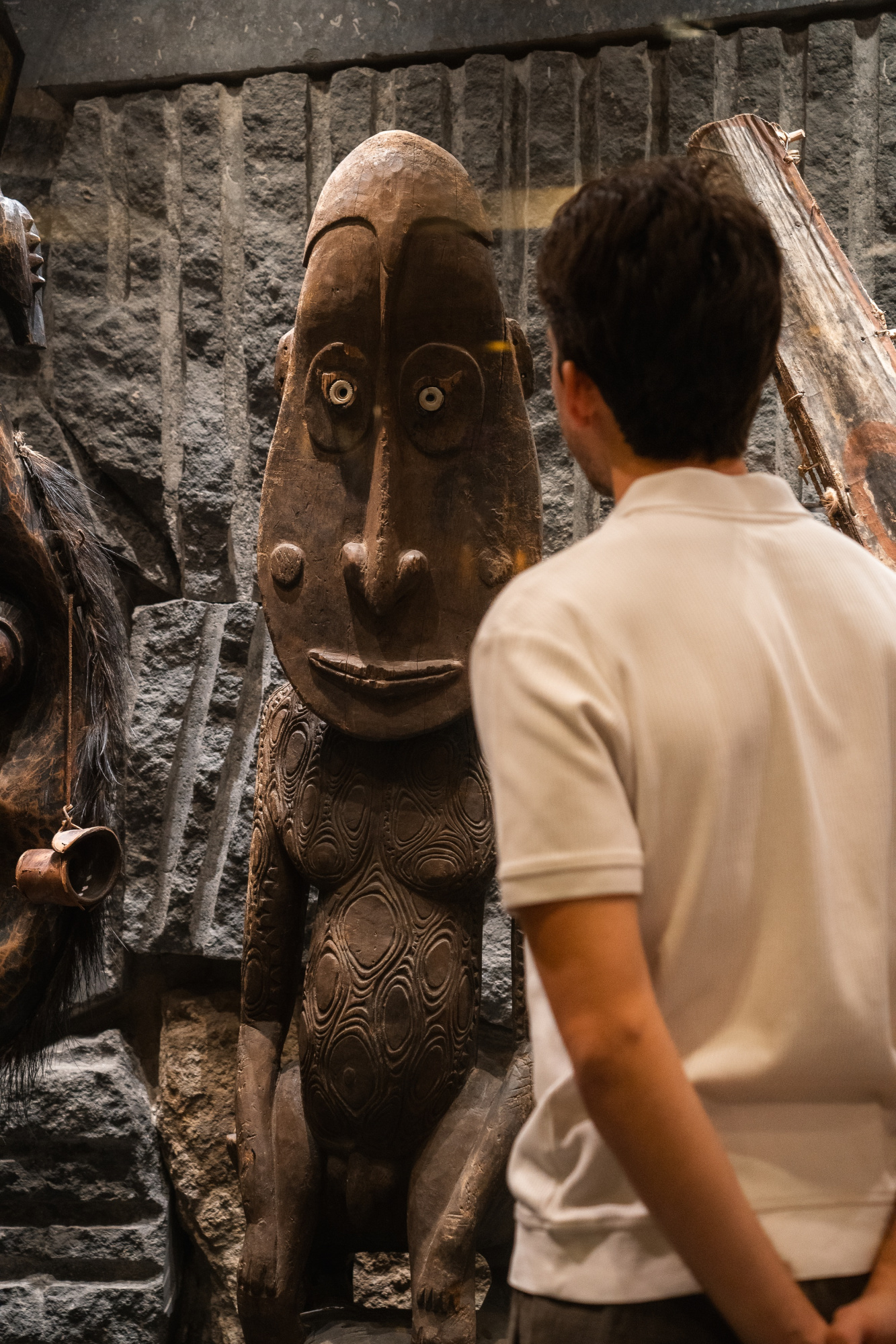 Una persona observa una escultura decorativa de estilo figurativo junto a una pared de piedra.