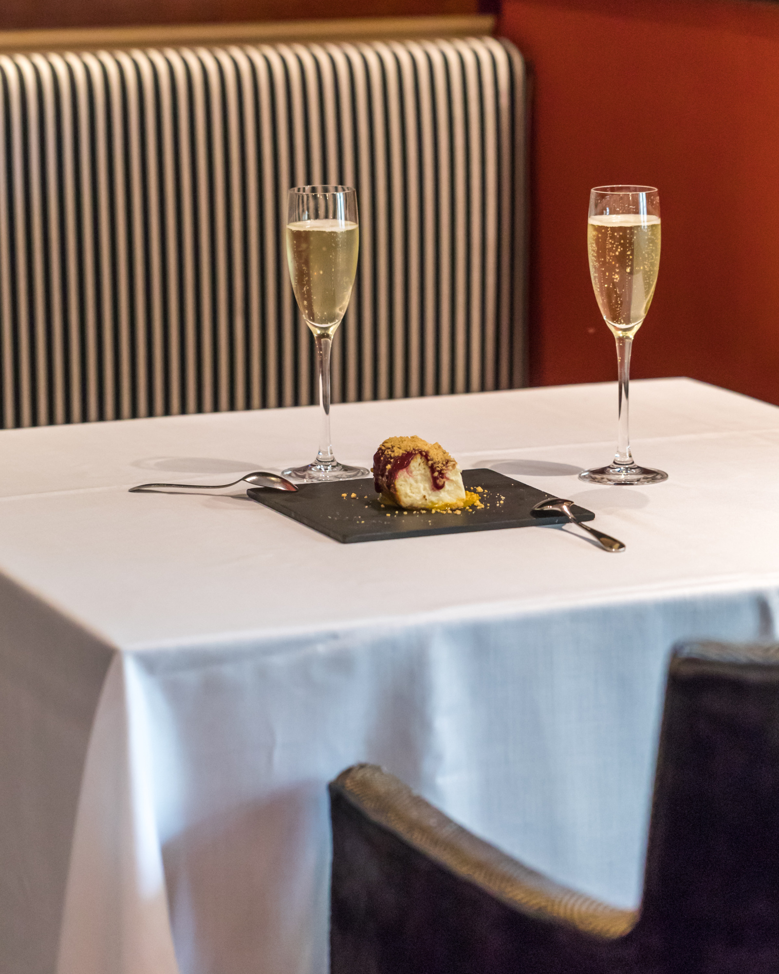 Sirven dos copas de champán y un postre en un plato sobre una mesa con mantel blanco.