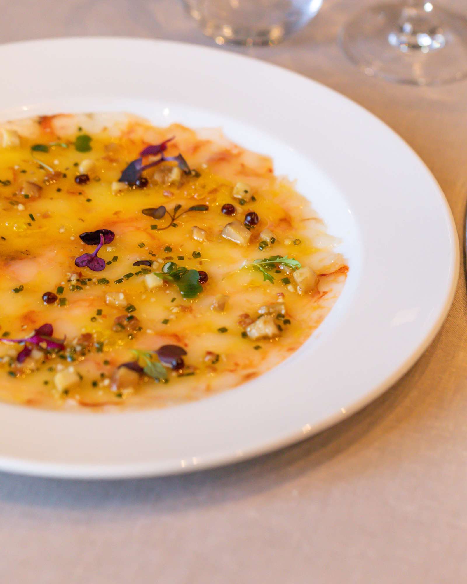 Sirve un plato blanco con crema amarilla y hierbas sobre una mesa.