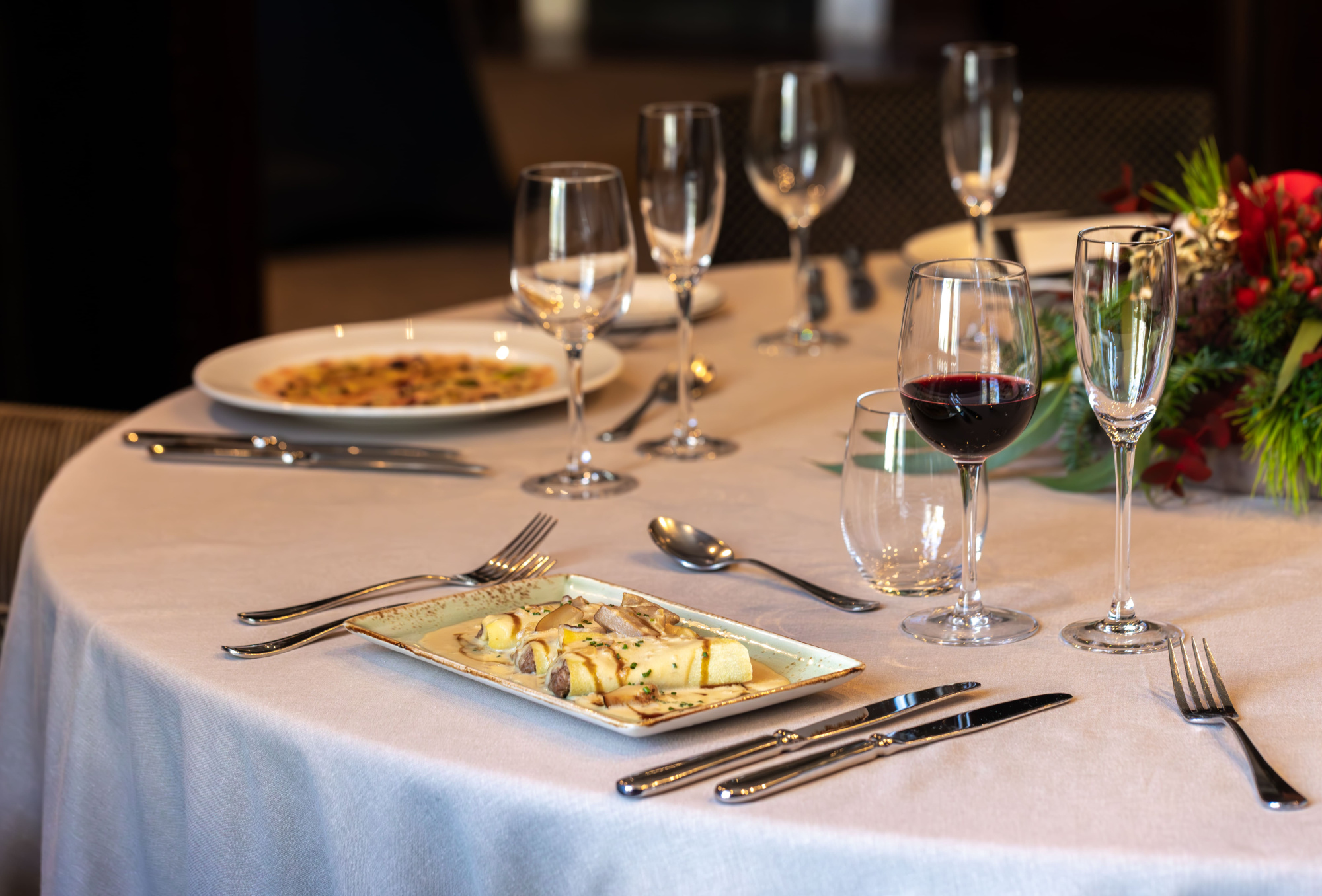 Mesa con platos, copas y cubiertos sobre un mantel blanco en un comedor.