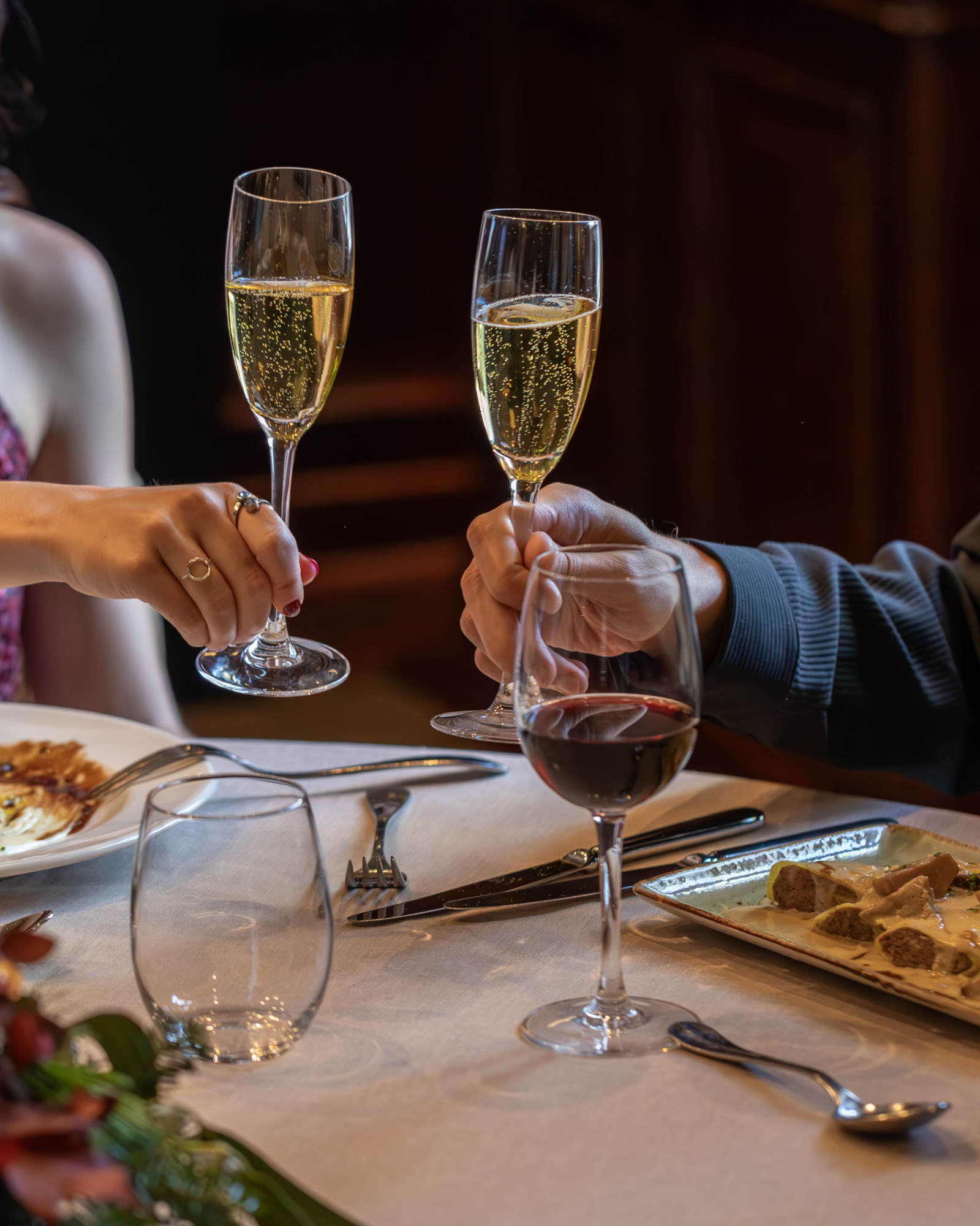 Varias personas brindan con copas de vino sobre una mesa con platos y cubiertos.