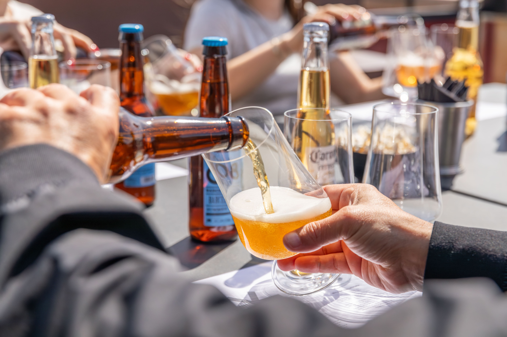 Varias personas brindan con vasos de cerveza sobre una mesa con botellas y vasos.