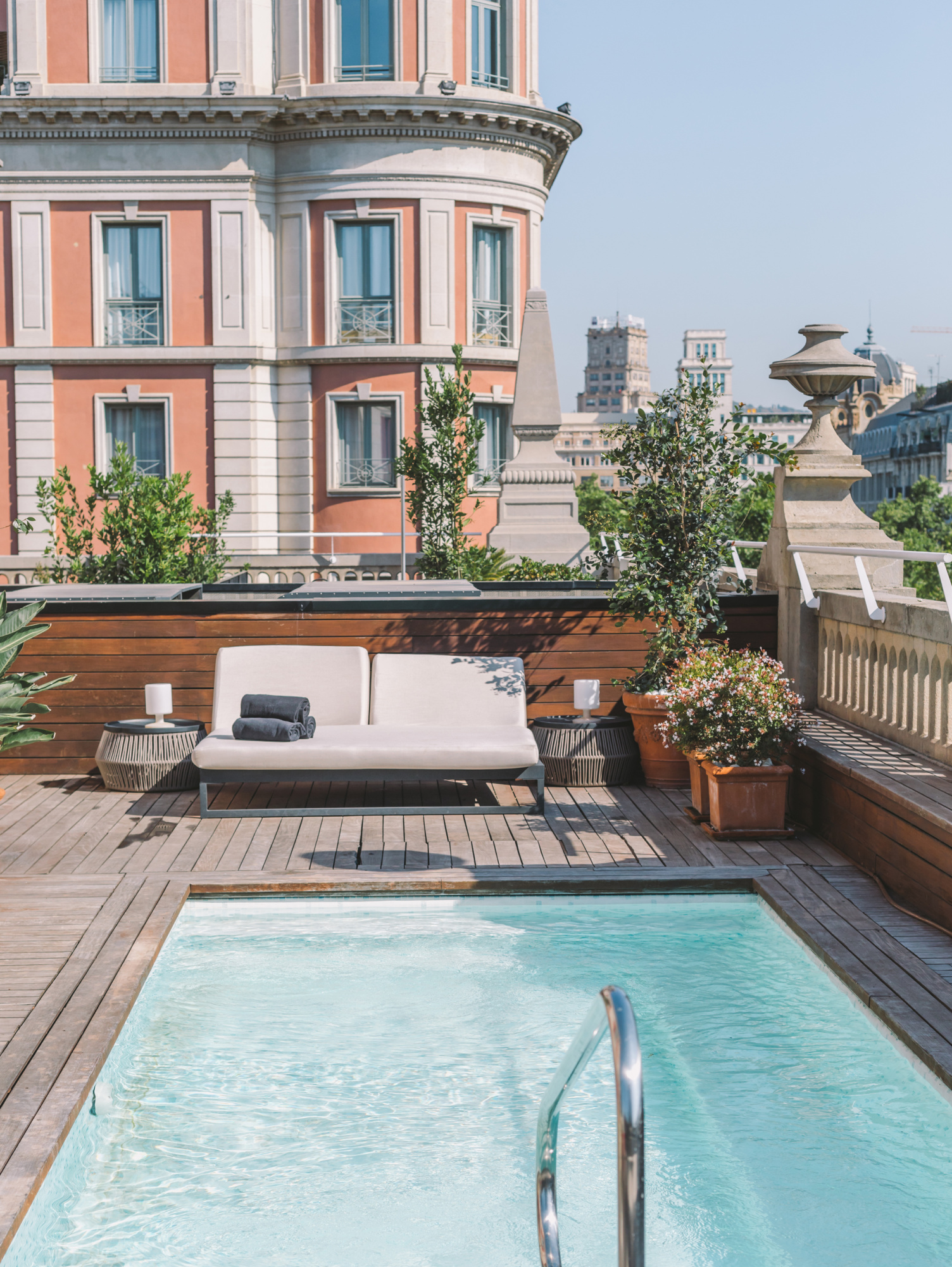 Se ve una terraza con una piscina privada de agua clara, tumbonas y plantas junto a un edificio de varios pisos.