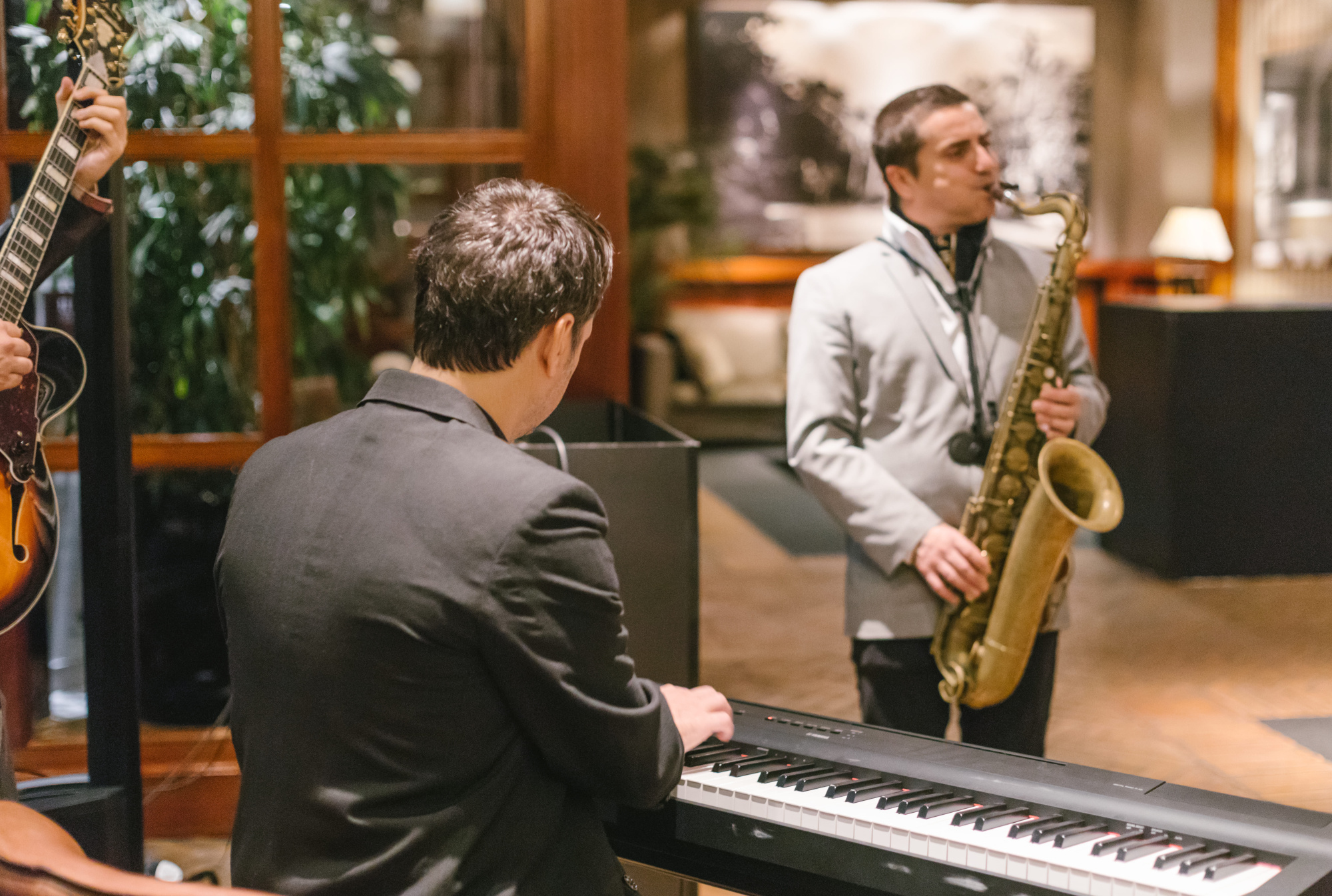 Un saxofonista y un pianista tocan en un escenario interior con un músico de guitarra al lado.