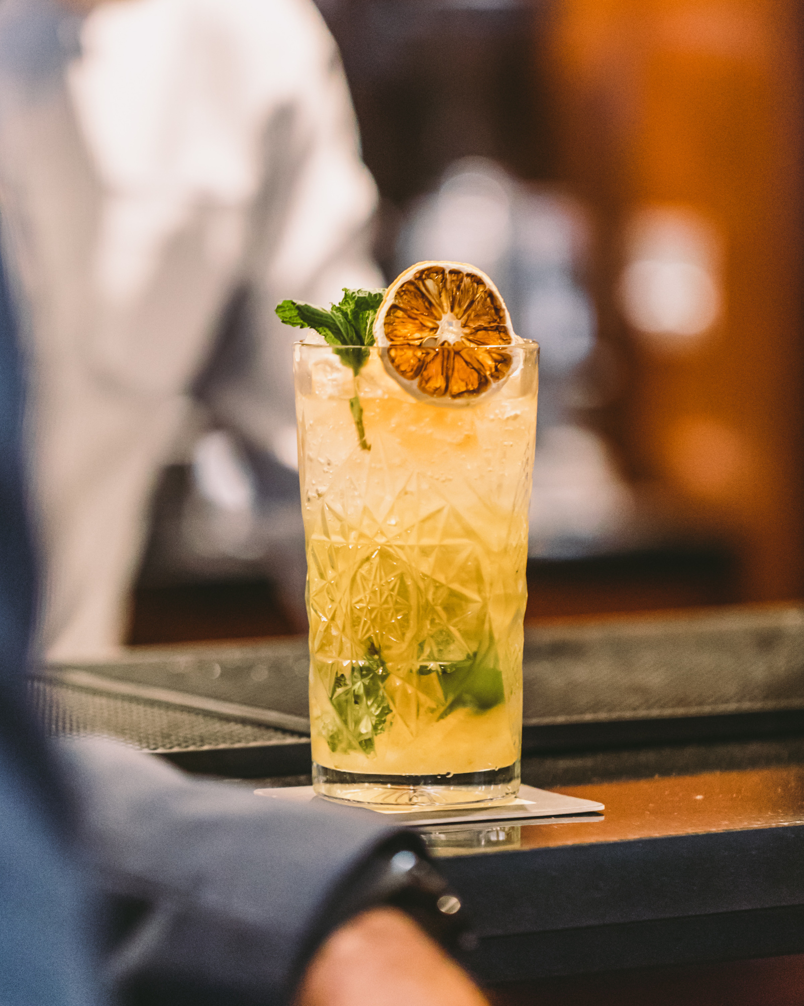 Sirven un cóctel con rodaja de naranja y hierbas sobre una barra de bar.