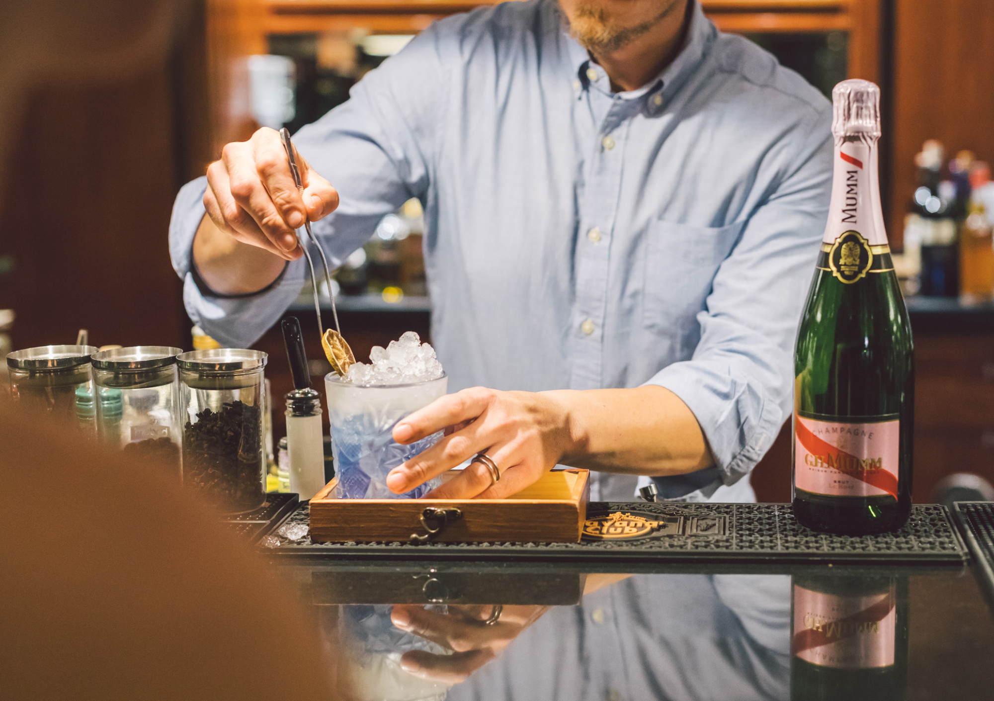 Un camarero prepara una bebida junto a botellas y vasos sobre una barra de bar.