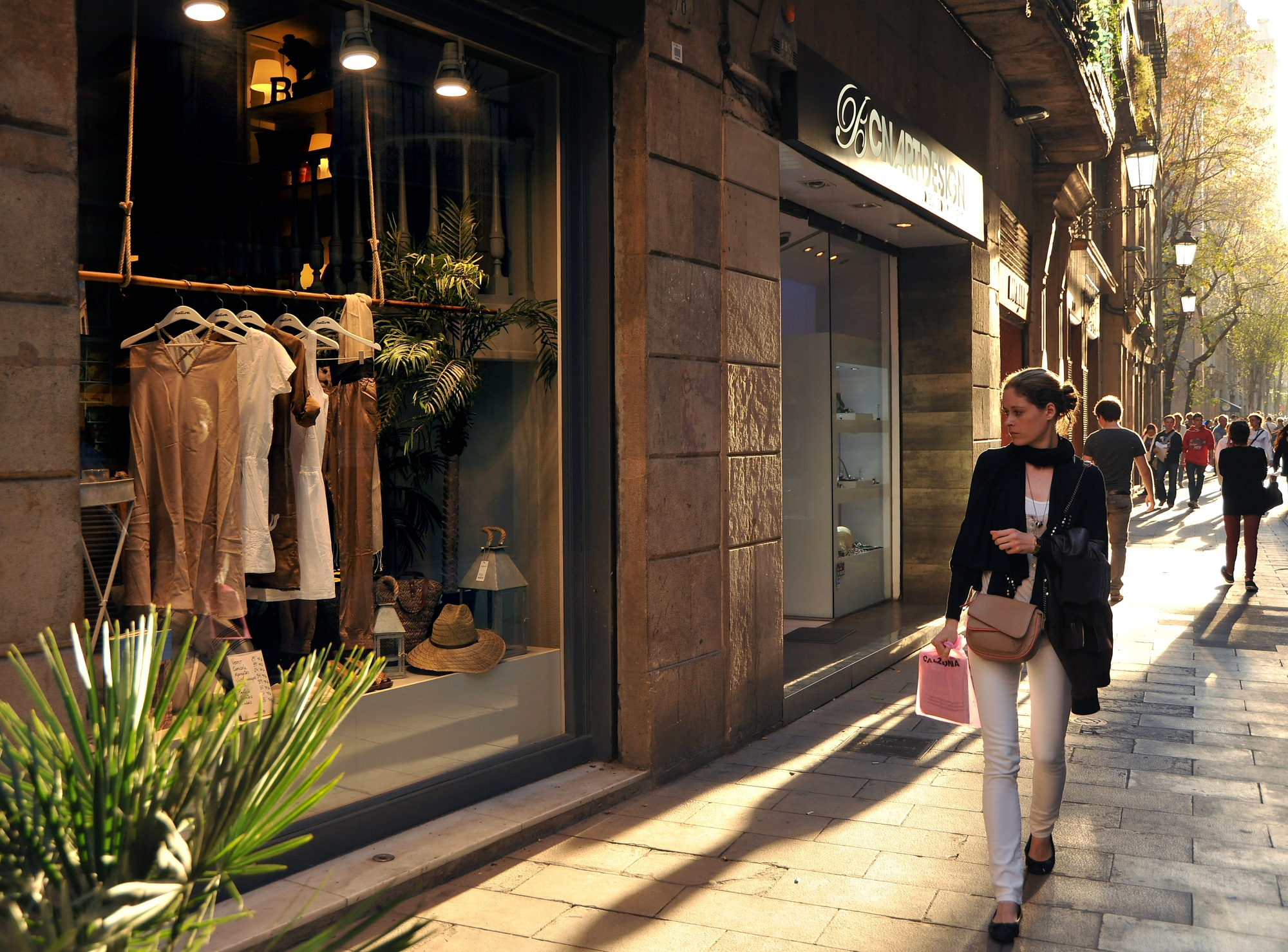 Se ve una calle peatonal con escaparates iluminados y personas caminando.