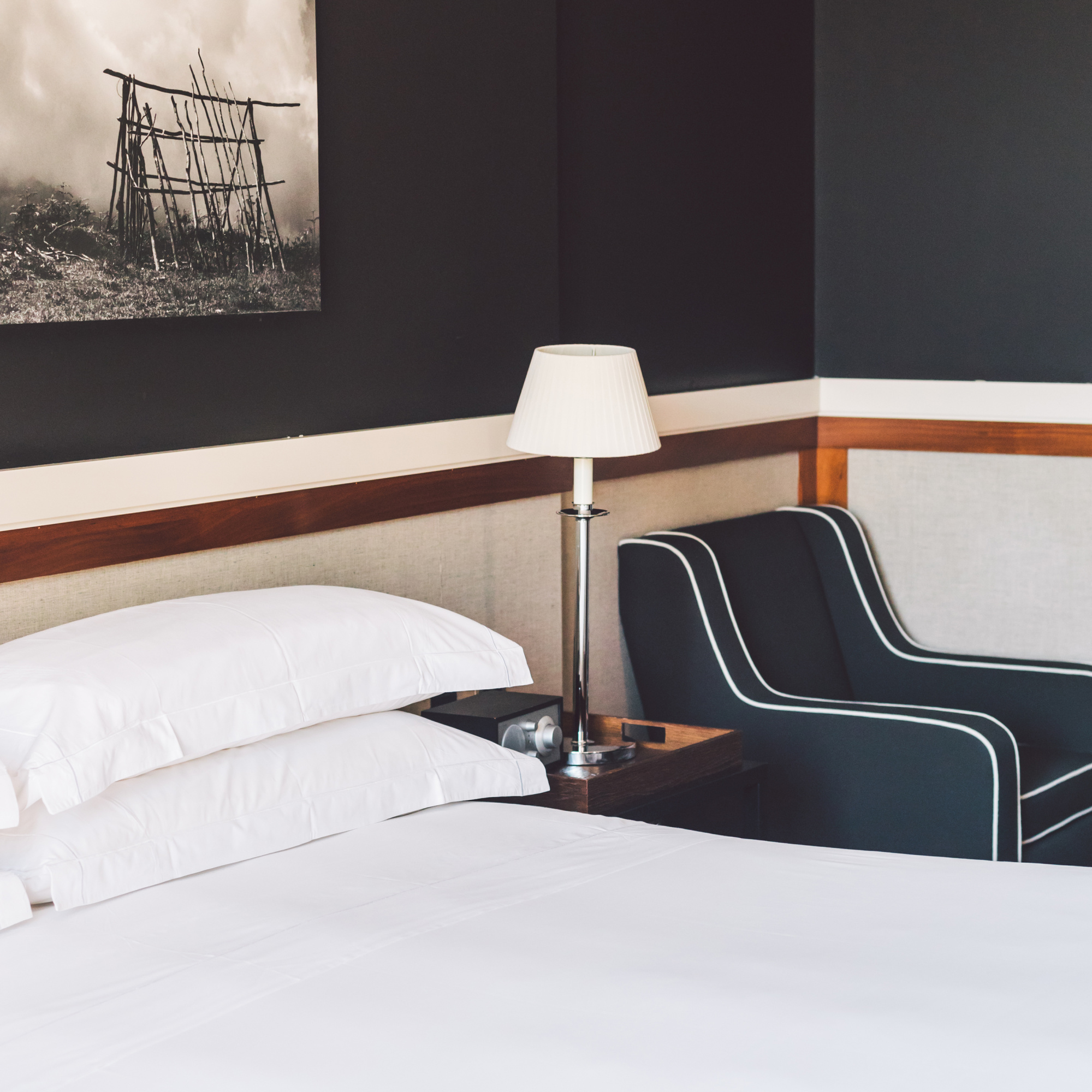 Se ve una cama con almohadas, un sofá y una lámpara de mesa sobre una mesita.