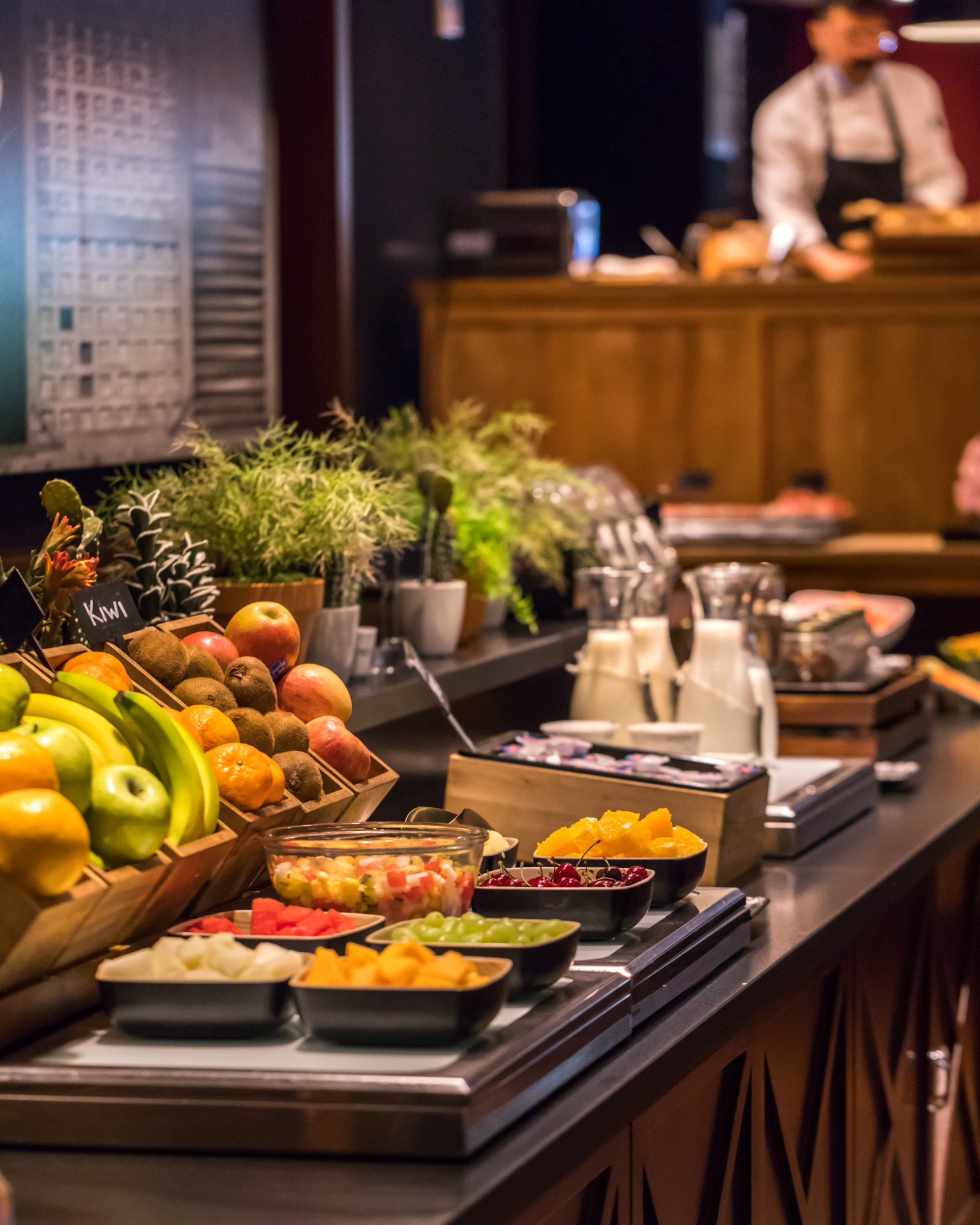 Una variedad de alimentos en un buffet de desayuno, incluyendo frutas, panes y otros productos, presentado en un entorno luminoso y acogedor.