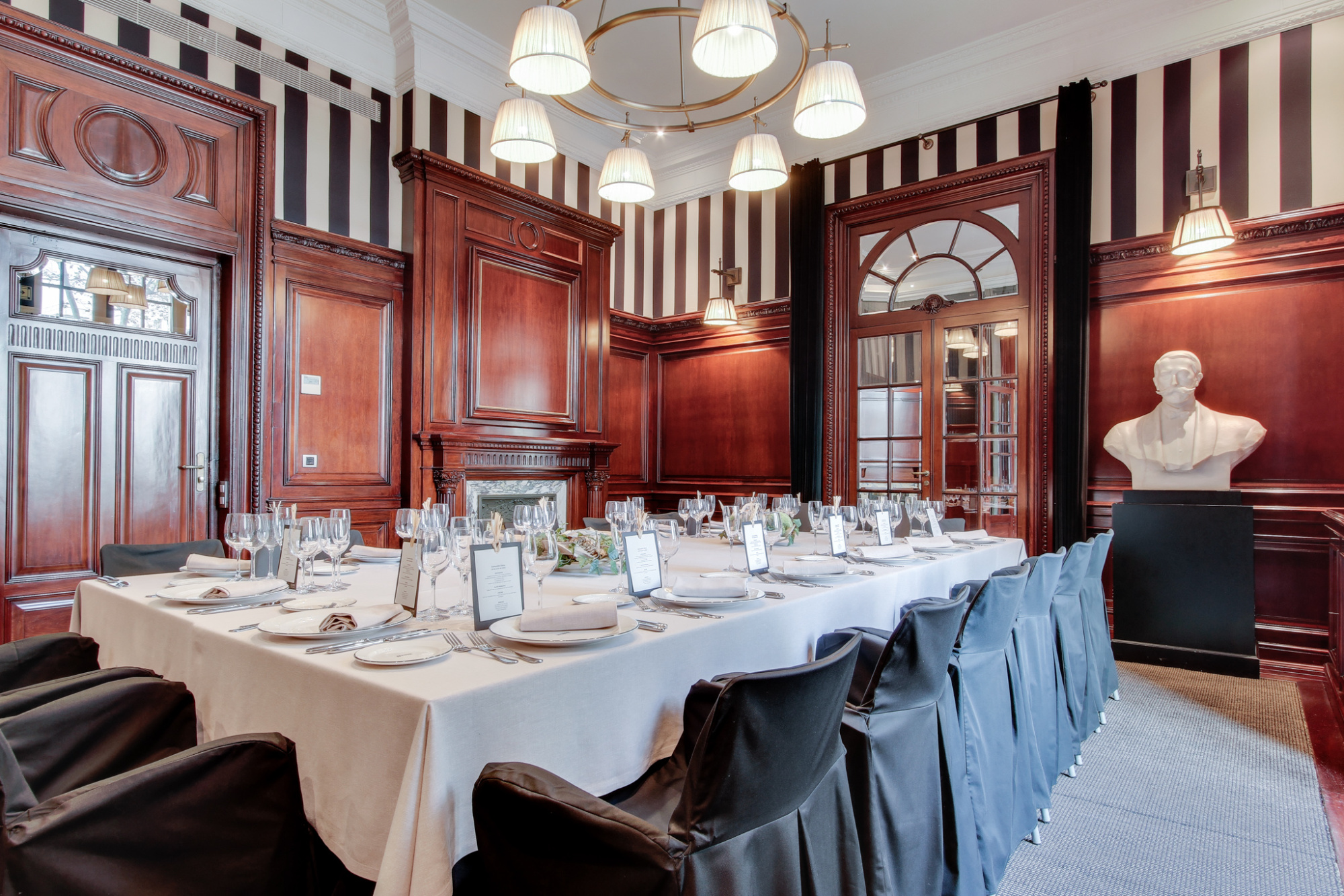 Un comedor elegante muestra mesas con manteles blancos y sillas alrededor, con lámparas colgantes y paredes de madera.