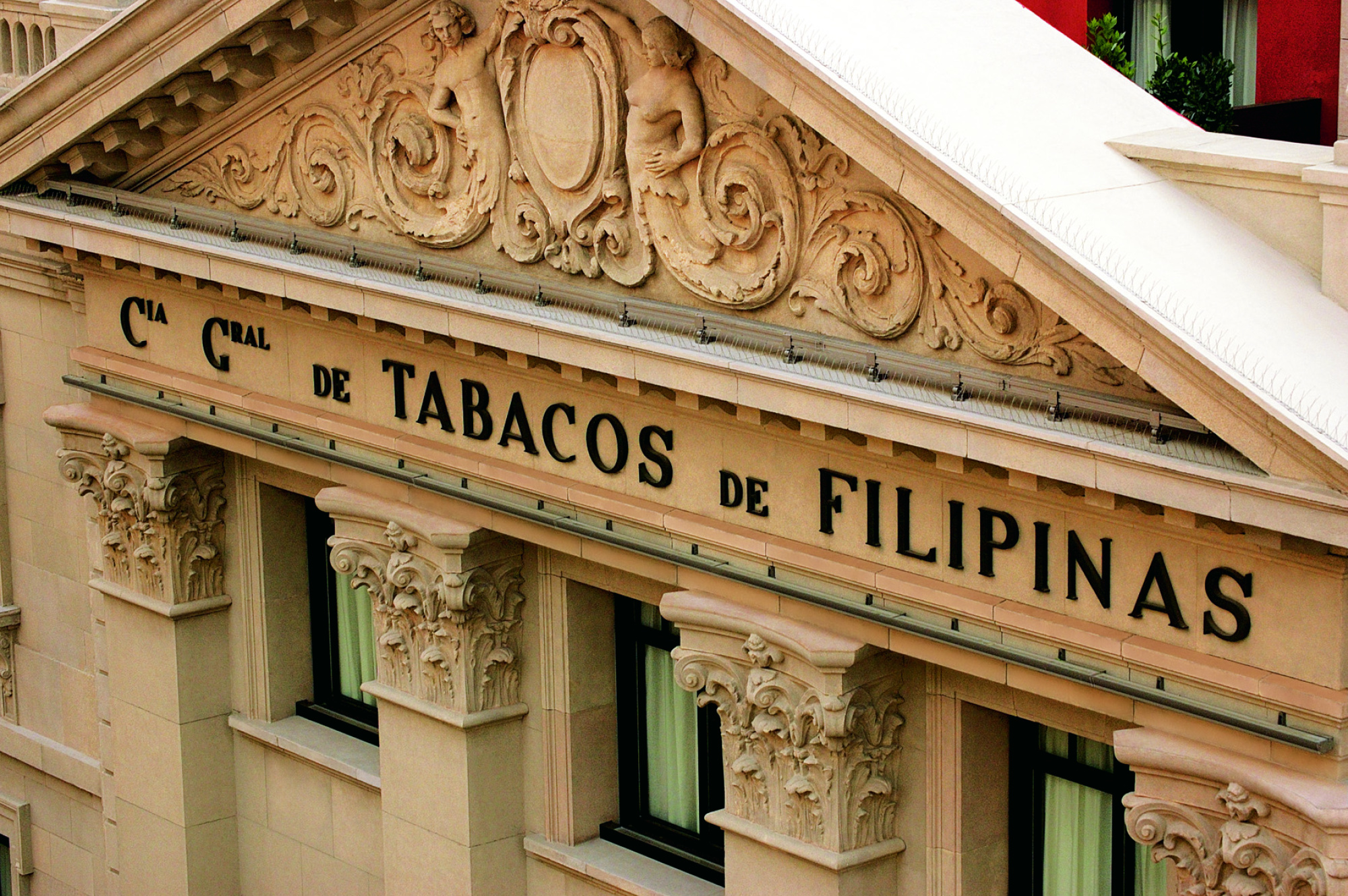 Se ve la fachada de un edificio con decoración tallada y un letrero que dice TABACOS DE FILIPINAS.