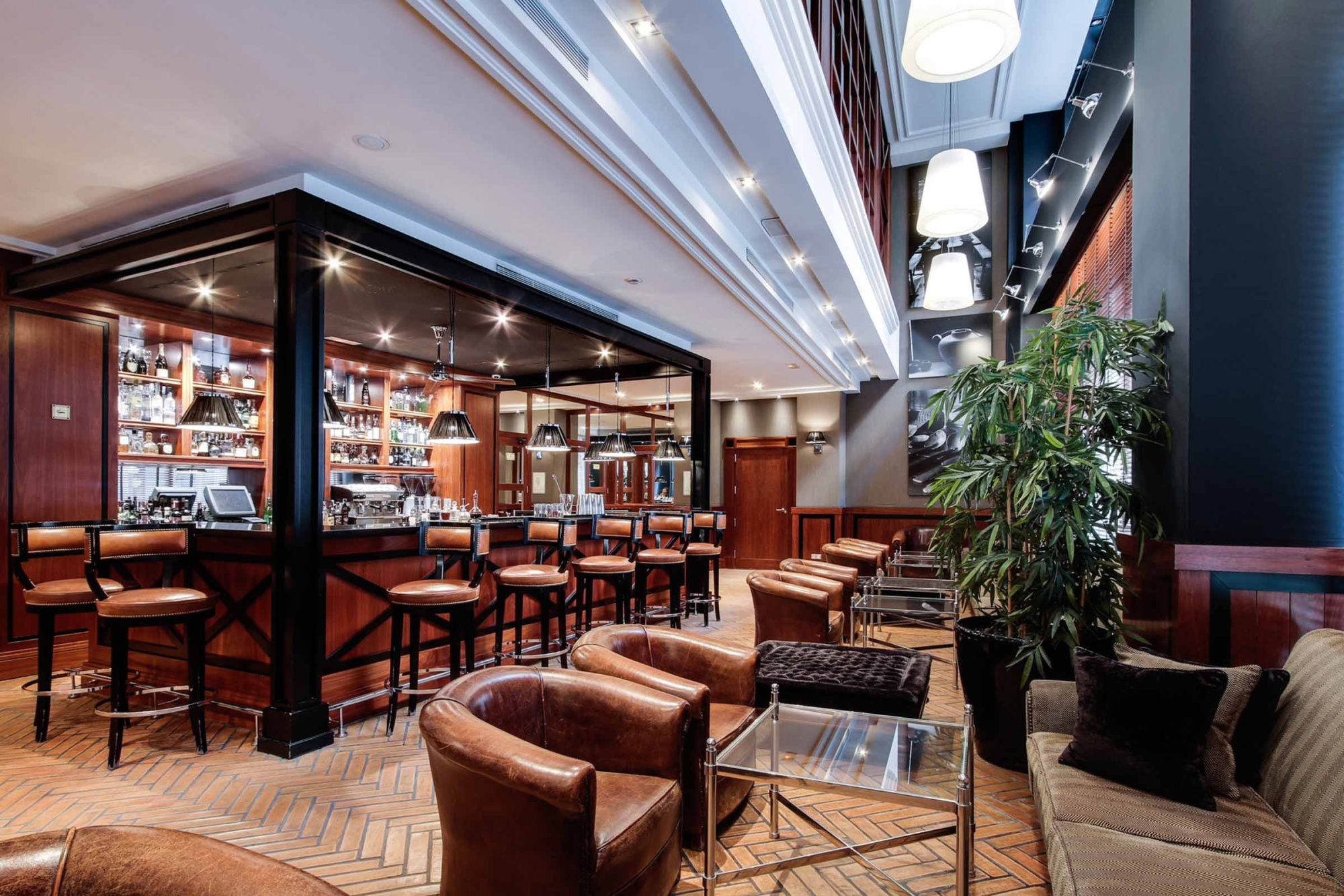 Se ve un bar interior con mesas, sillas y estanterías con botellas, junto a una zona de asientos.