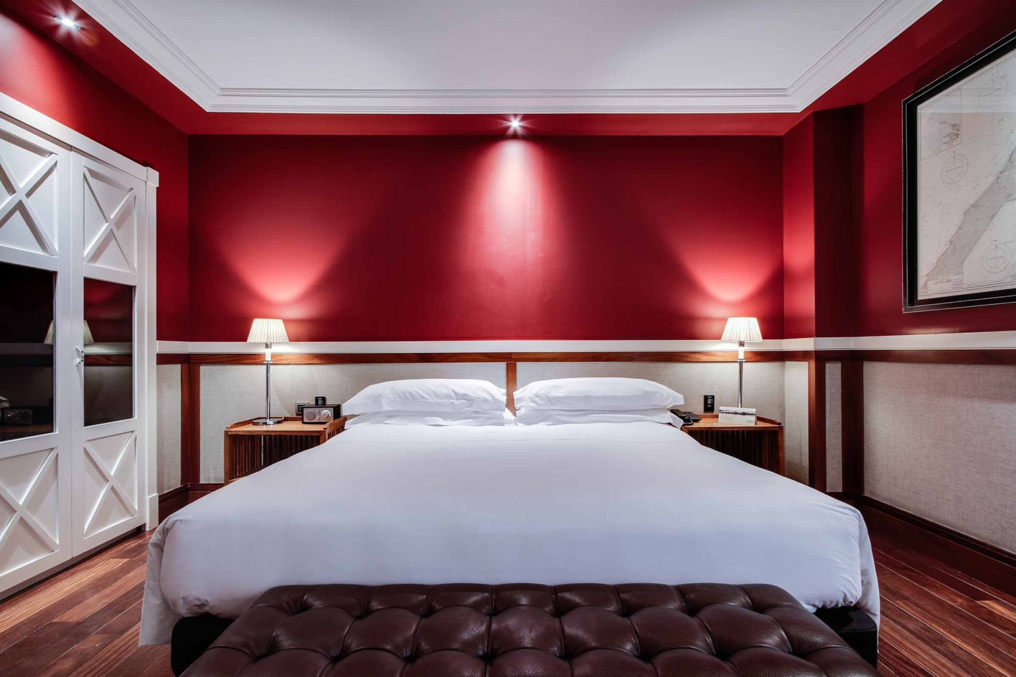Se ve una cama doble con cabecero acolchado, dos mesitas y lámparas en una habitación con paredes rojas.